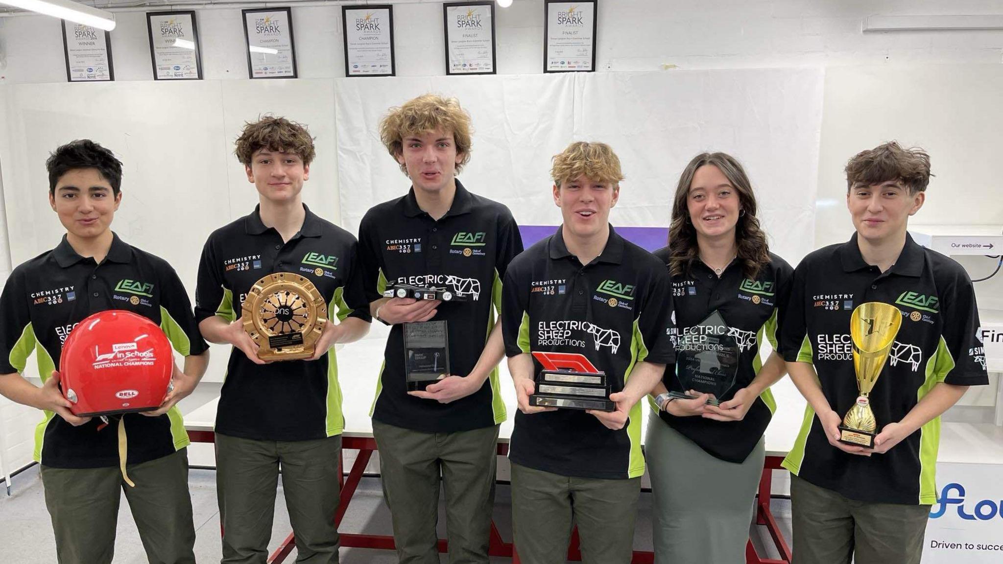 Six children wearing black and green shirts are smiling, they are stood side by side