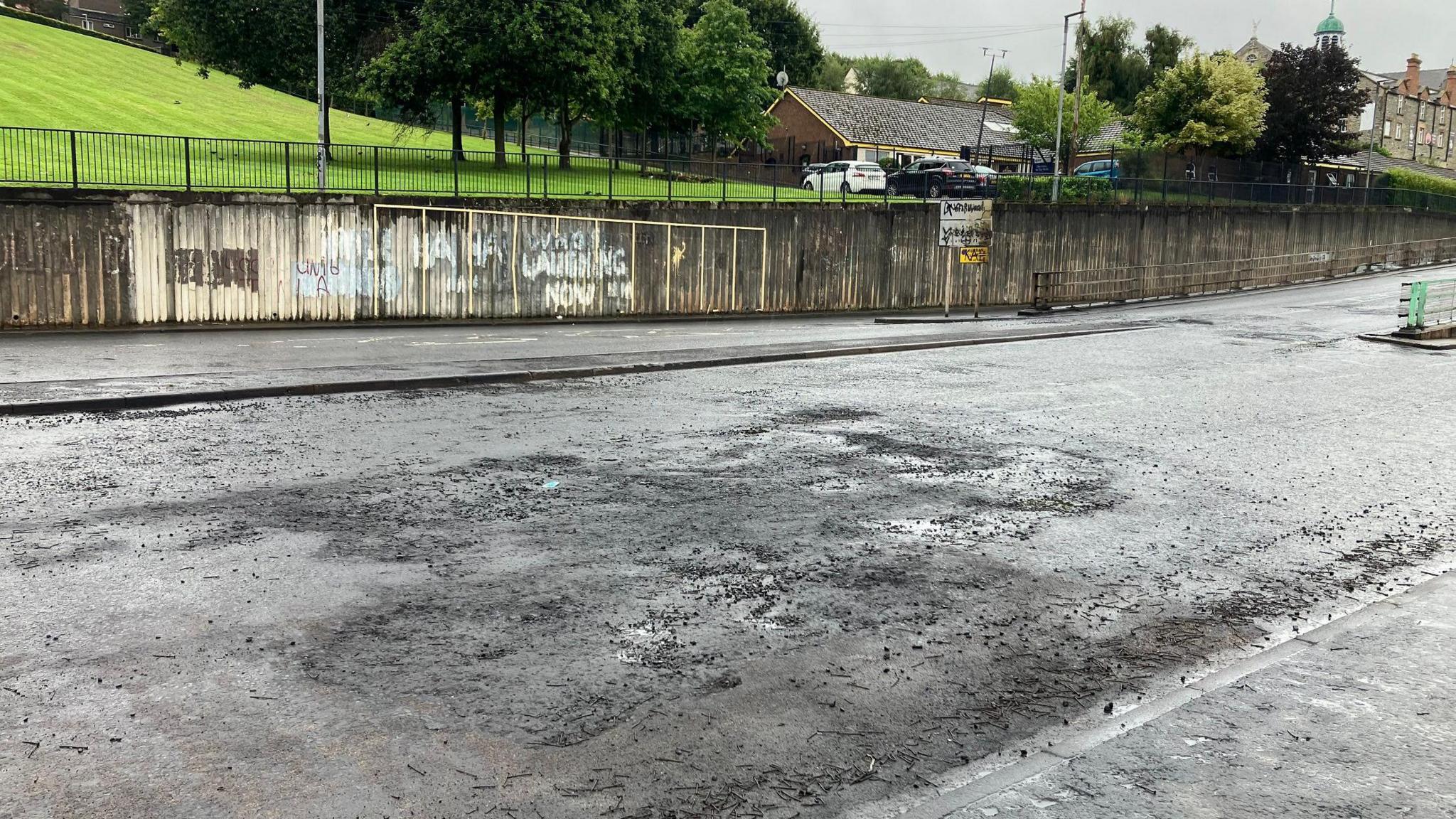 a road surface damaged by fire. Scroch marks and indents are seen on a road surface.