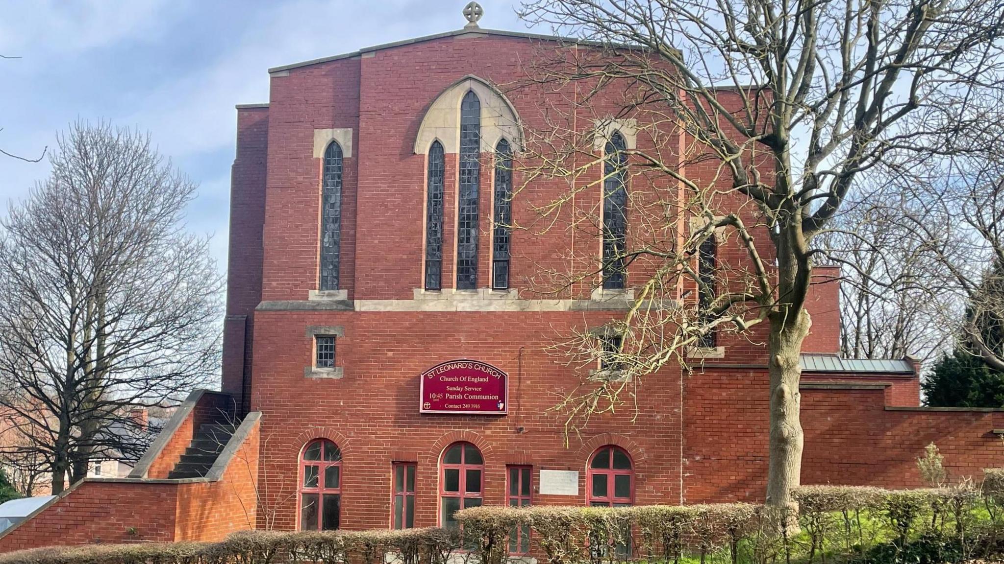 A tall red-brick church building surrounded by trees.