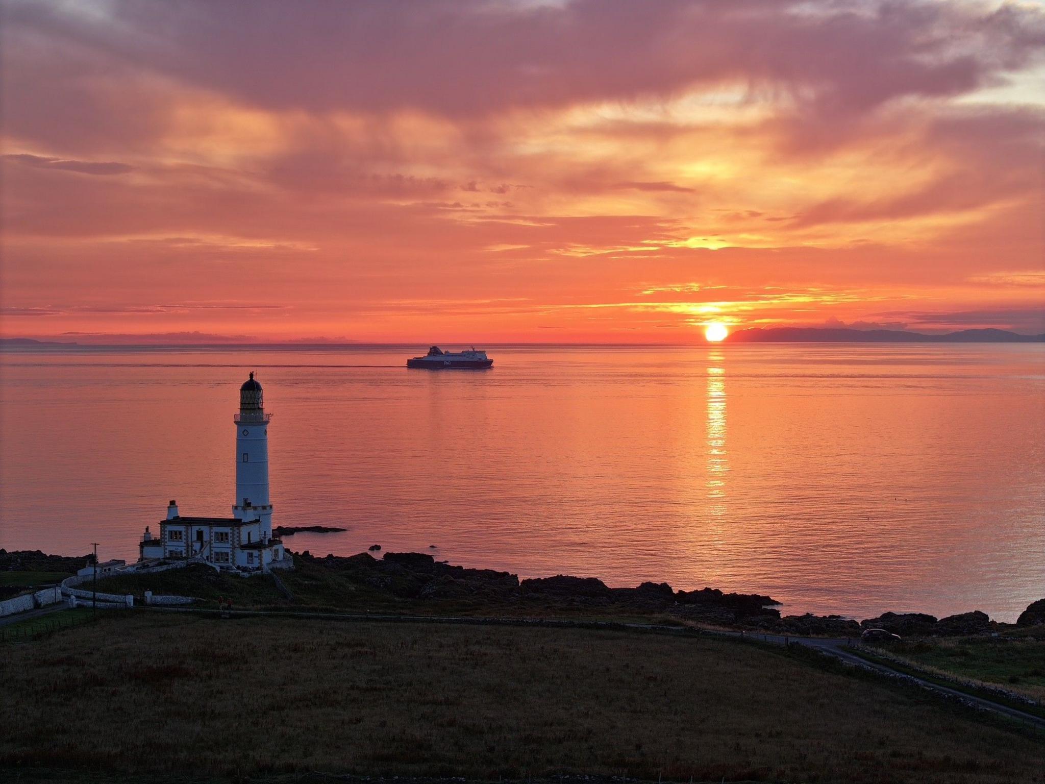A vivid orange and yellow sun setting in the distance with a lighthouse in the foreground