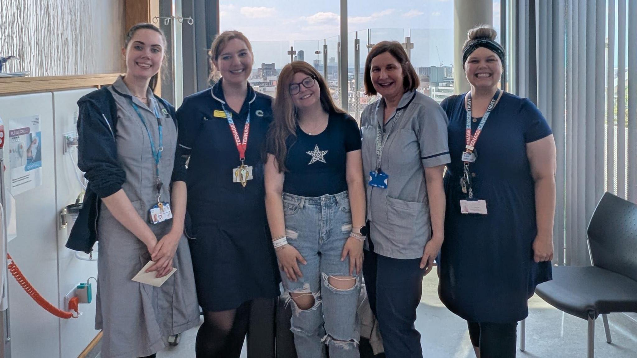 Daisy, person ifanc o Ynys Môn, yn sefyll gyda grŵp o nyrsys mewn ward ysbyty yn Lerpwl yn ystod ei thriniaeth canser