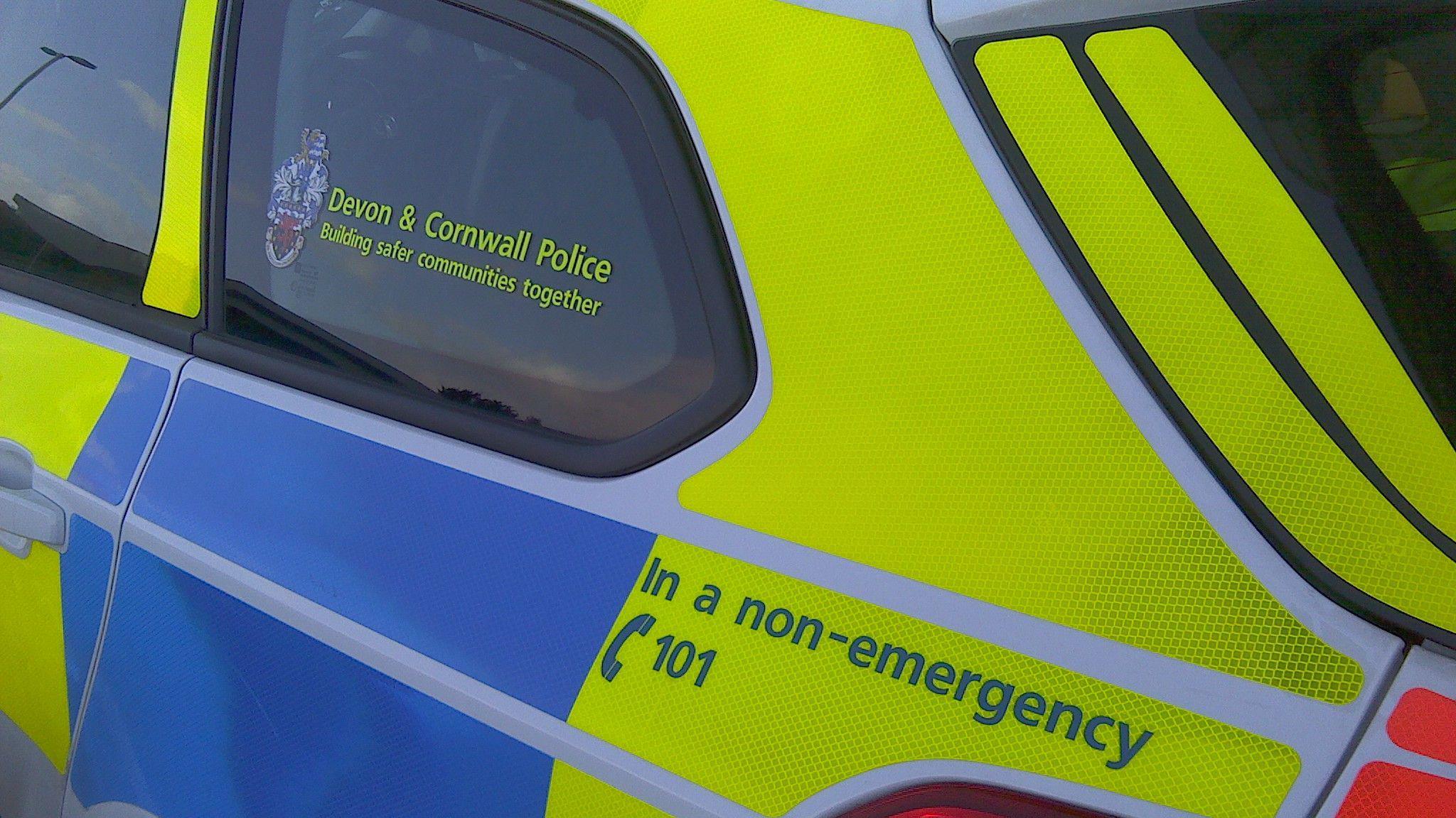 Close up of Devon and Cornwall Police car. The car has yellow and blue reflective stickers. A sign on the window states Devon and Cornwall Police Building safer communities together.