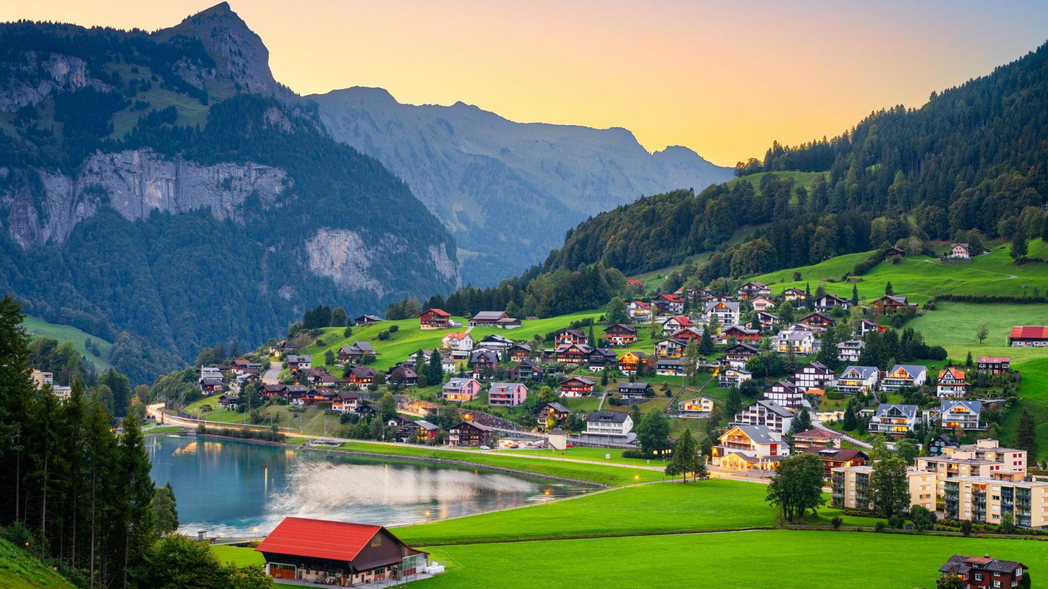 A landscape photo of the town of Engelberg. There are mountains in the background, and in the foreground chalets are next to a lake.