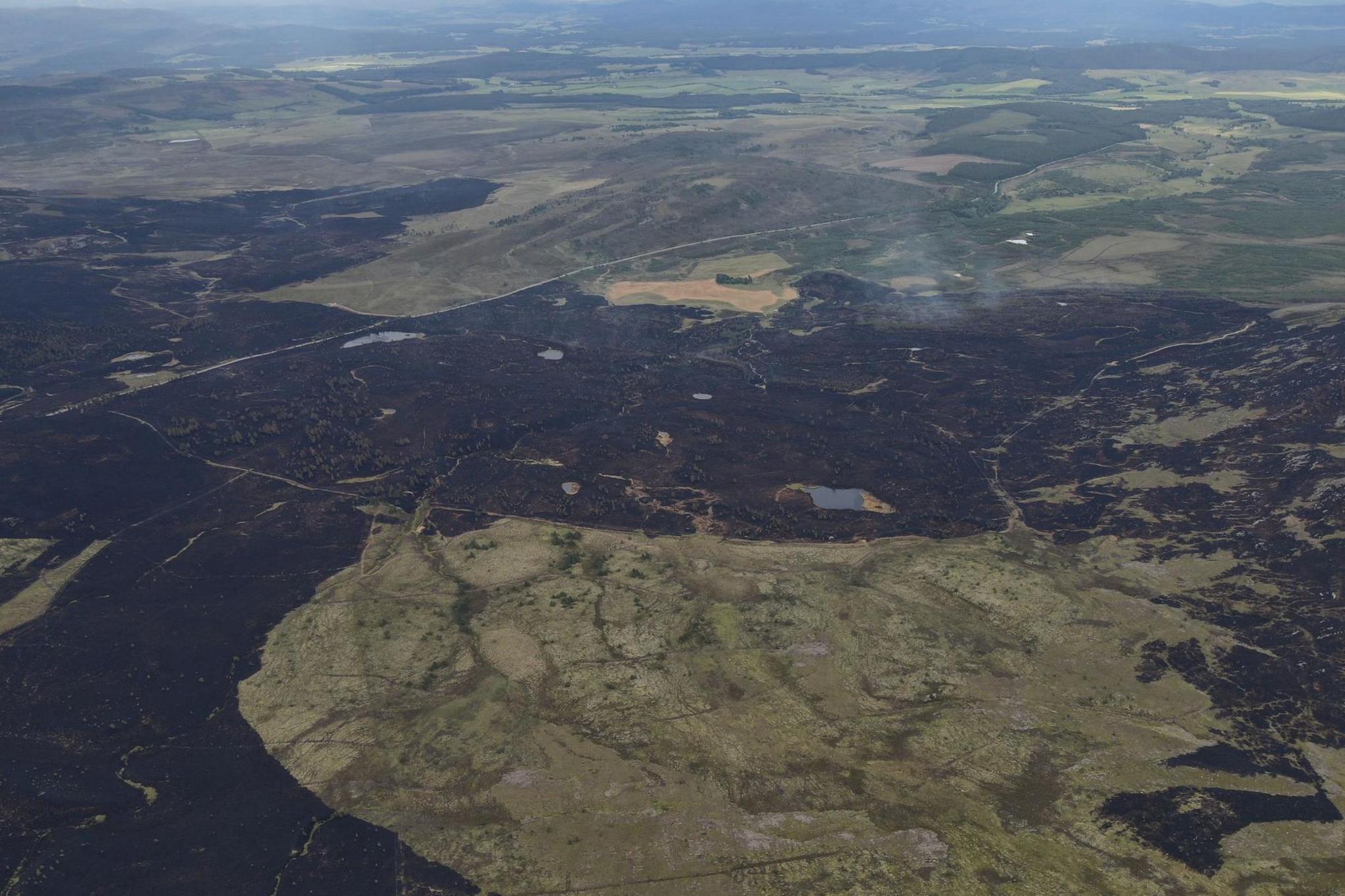An image taken by a drone shows an area of burned moorland. Smoke rises from a corner of the affected land. The rest of the landscape is a patchwork of moor, forestry and farmland.