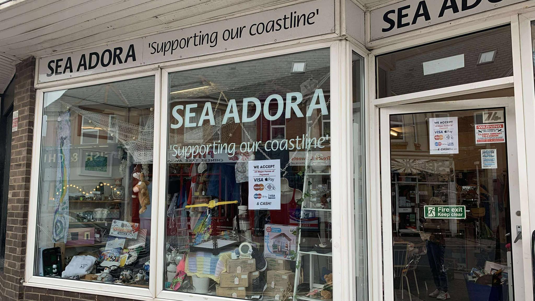 The front of Sea Adora which has a big window on the left and a door to the right. The words 'Sea Adora' is written on the window and below it has the words 'supporting our coastline'.