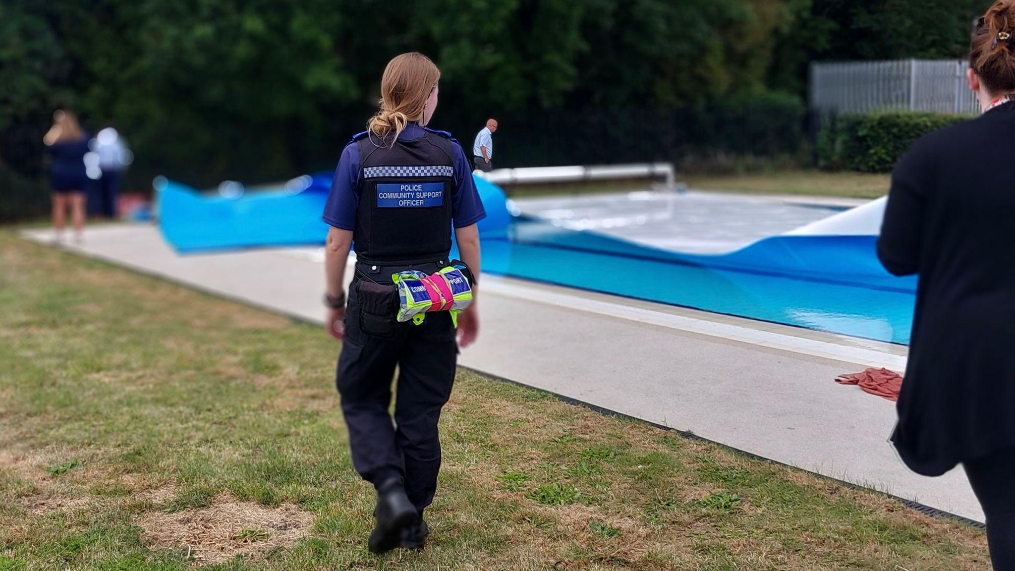 A woman TVP officer walking beside the Abbey Meadows outdoor pool. People can be seen around the pool in the distance, handling its covers.