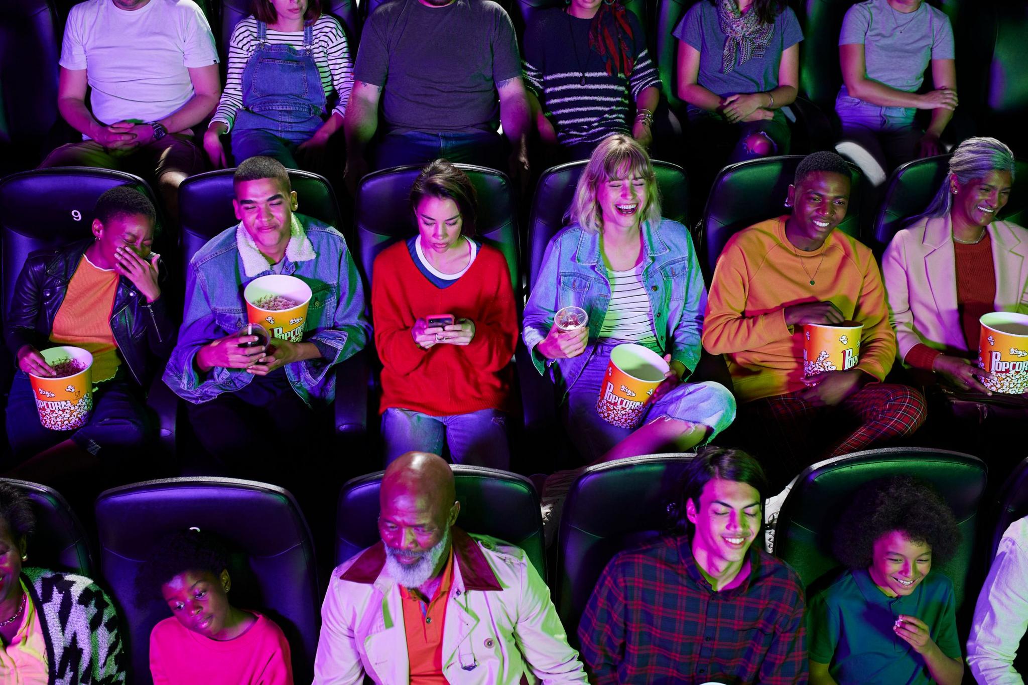 Aerial view of people in the cinema with a woman sat in the middle of the row using her phone while others watch the film 