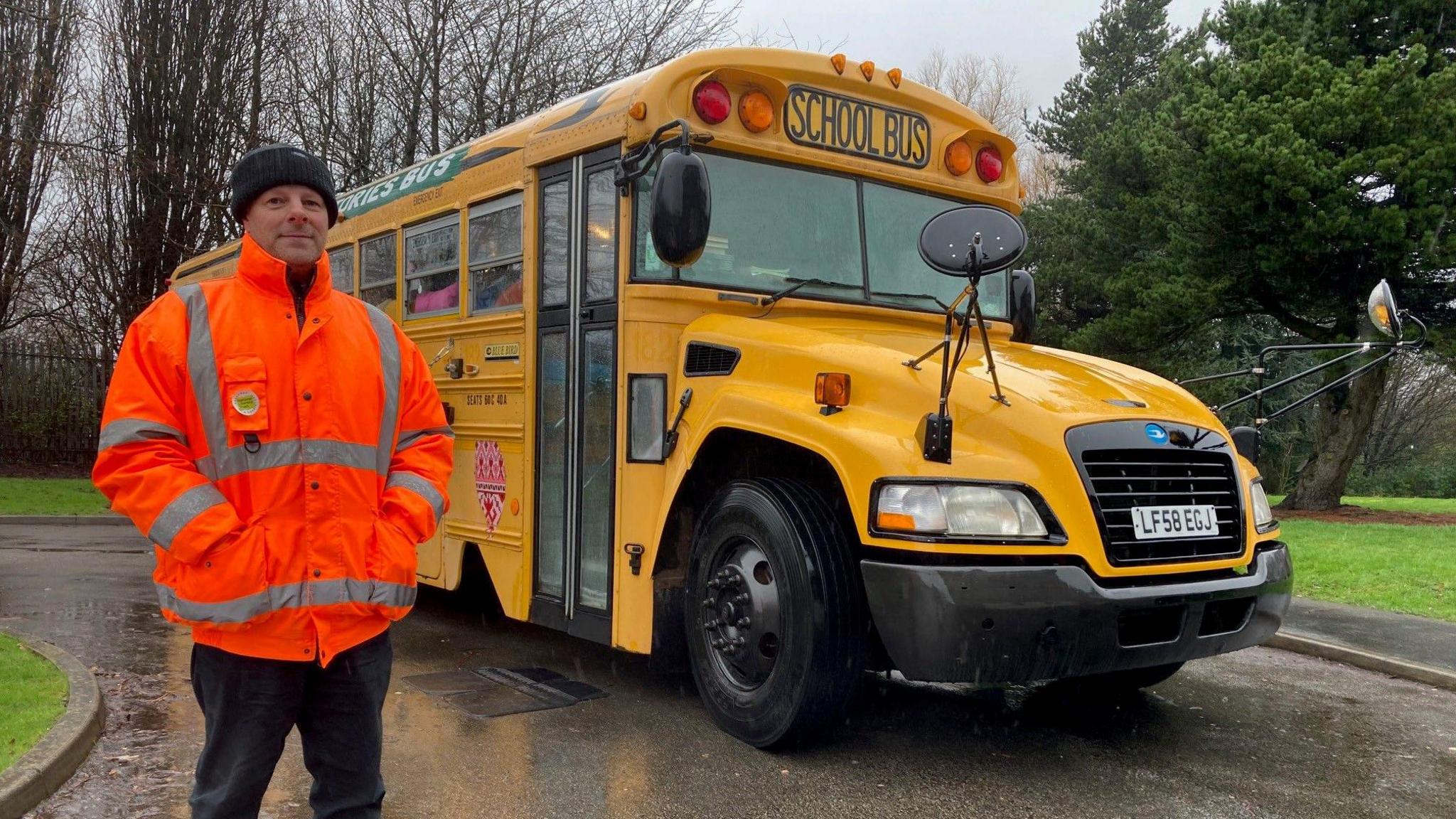 Driver standing next to a yellow US school bus