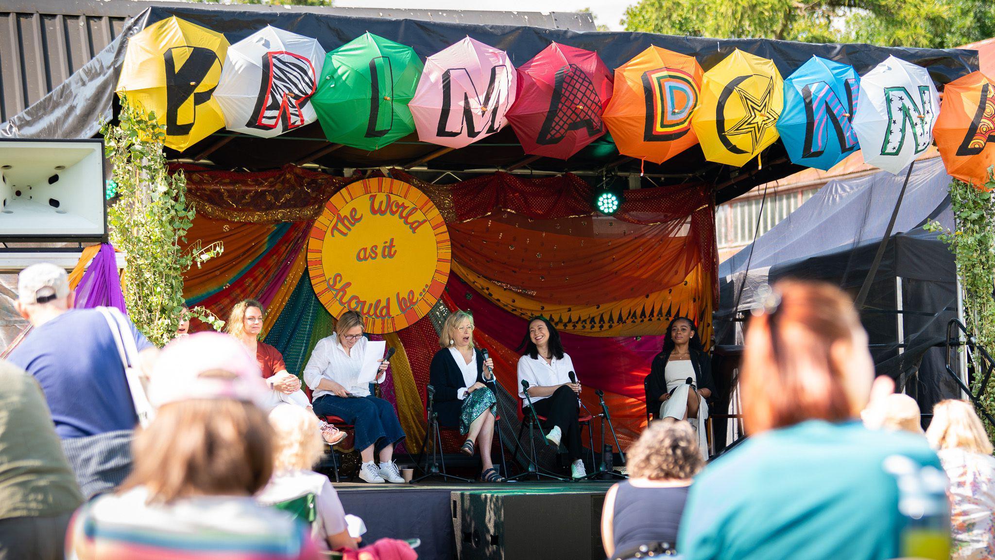 A view of the Primadonna Festival stage during a previous event. Five women sit on stage talking to an onlooking crowd.