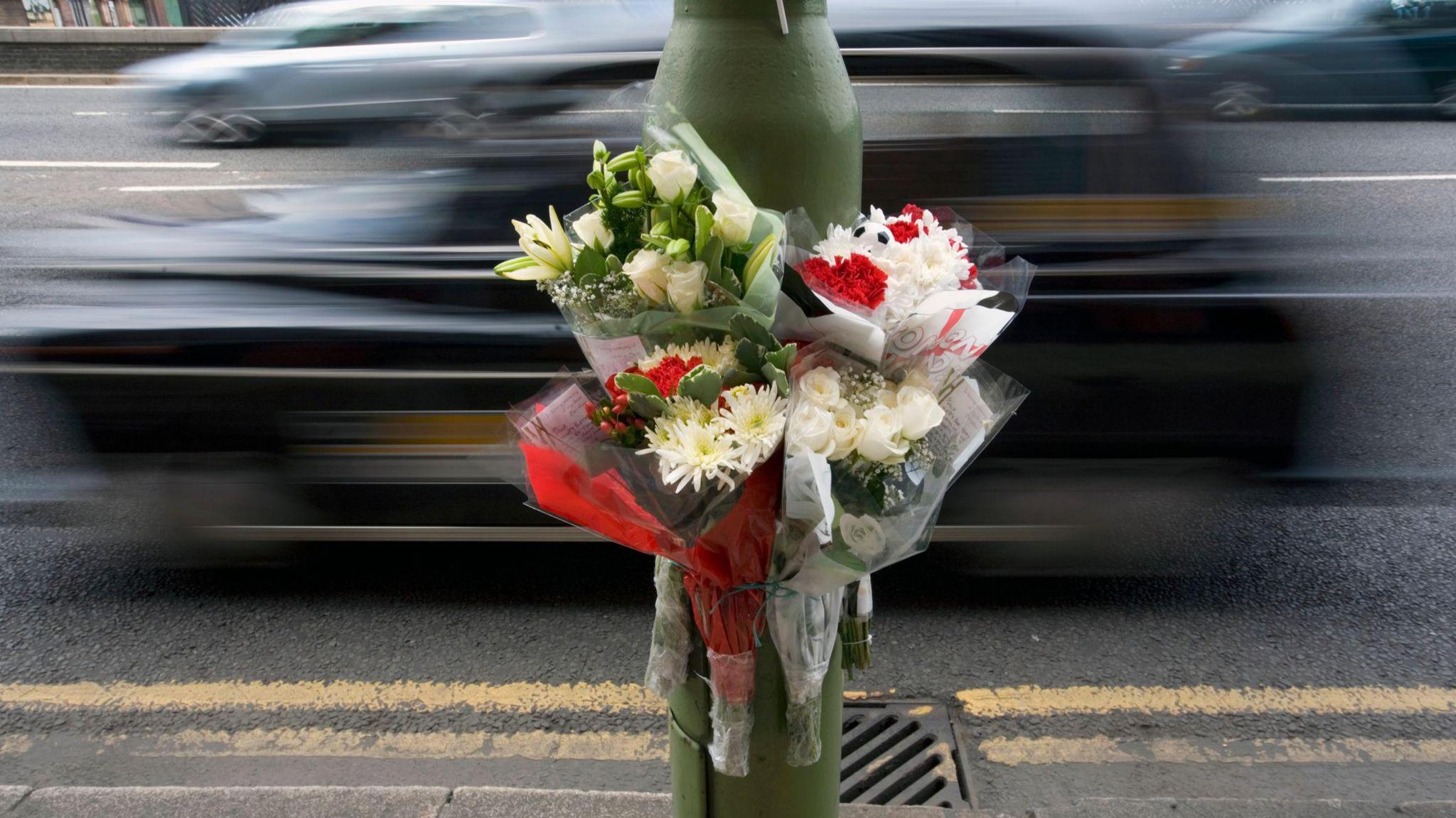 A bouquet of flowers attached to a lamppost next to a busy road