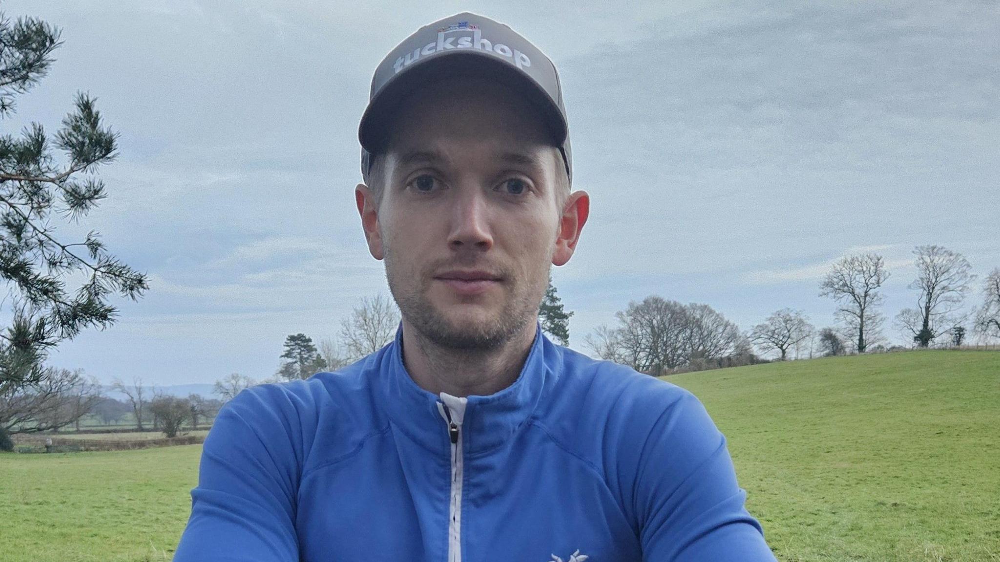 Image of Jacob James in a blue top with a white front zip. The words 'Whole Moo World' are on his top. He is also wearing a grey baseball cap 