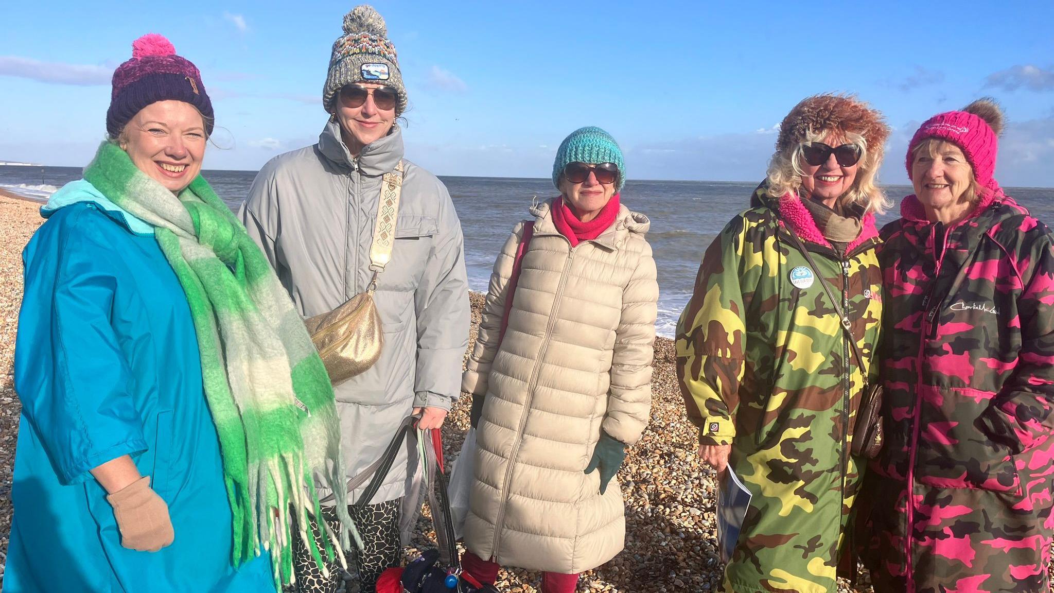 Five women wrapped up in coats and hats standing on the shingle beach at Deal with the sea behind them