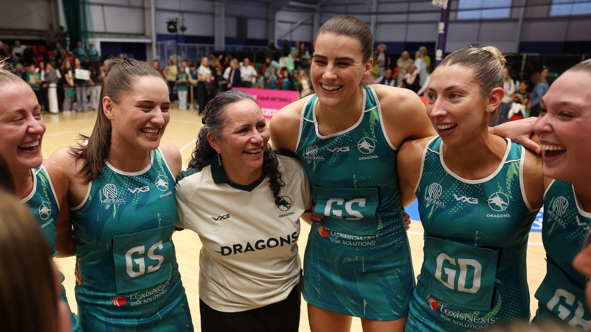 Dragons players link arms on courtside with Reigna Bloxham