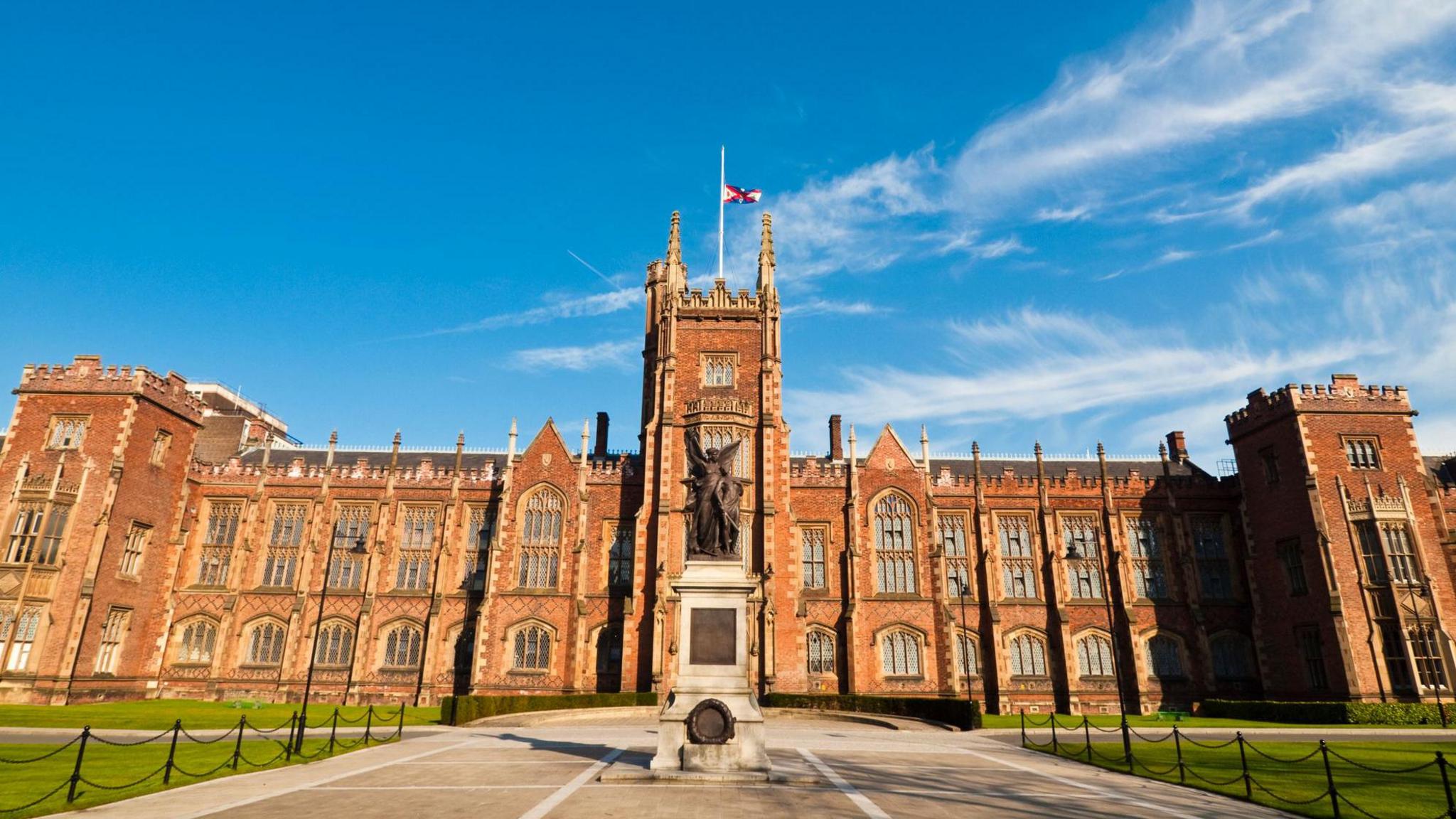 The exterior of Queen's University Belfast, a red brick building. There is a blue sky in the background. 