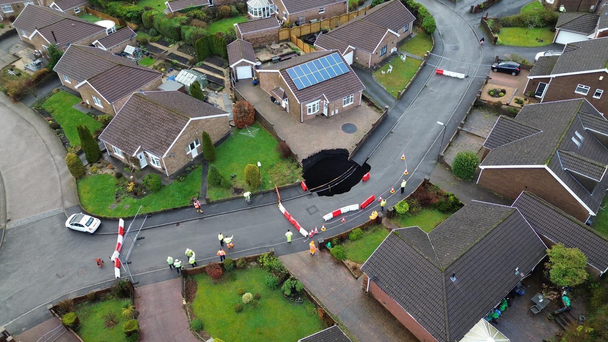 An aerial view of the housing estate with homes, the sink hole and emergency services visible