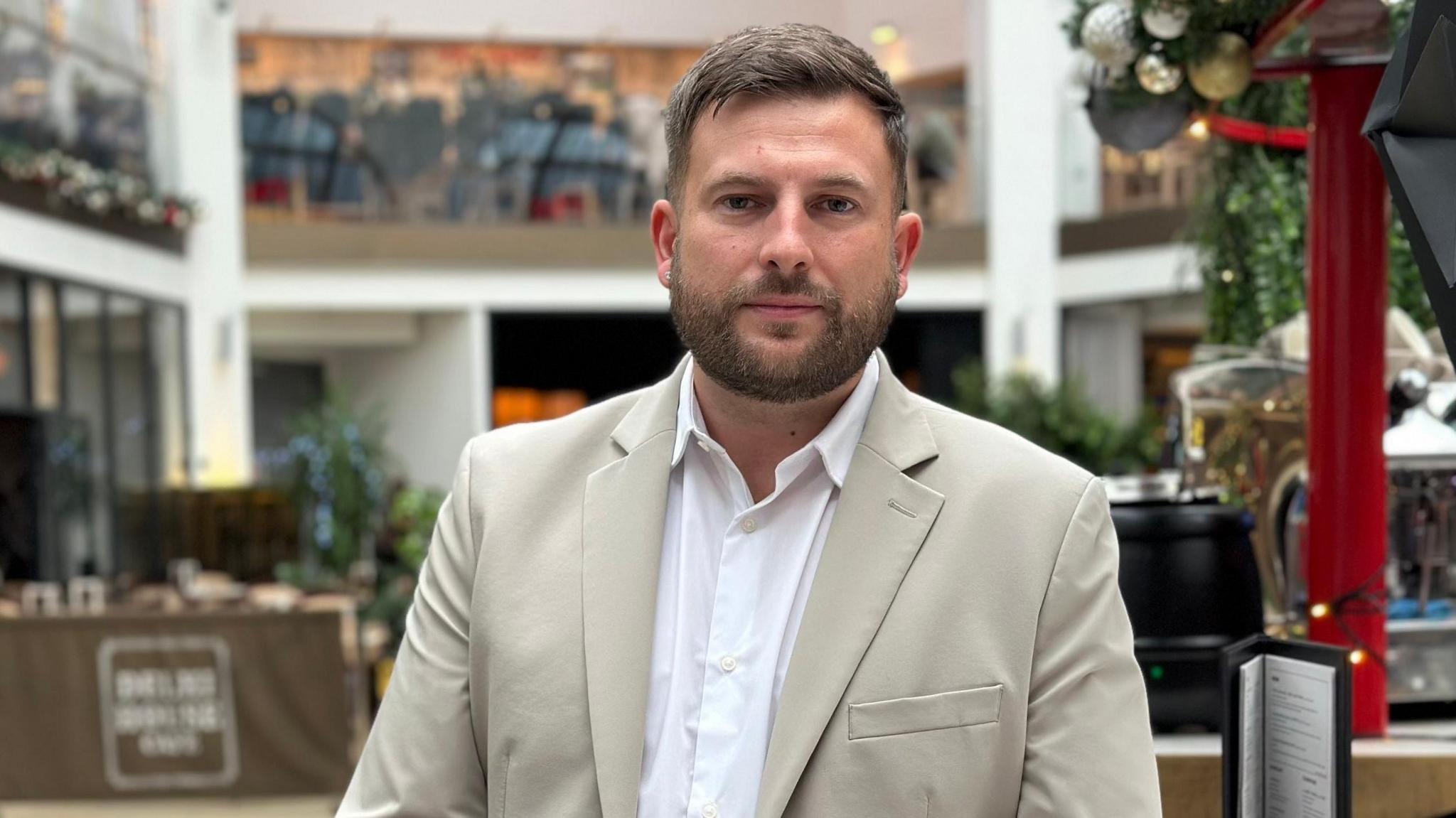 James Stott, general manager of Garten Bar, wearing a cream suit jacket, white shirt, sitting in his bar