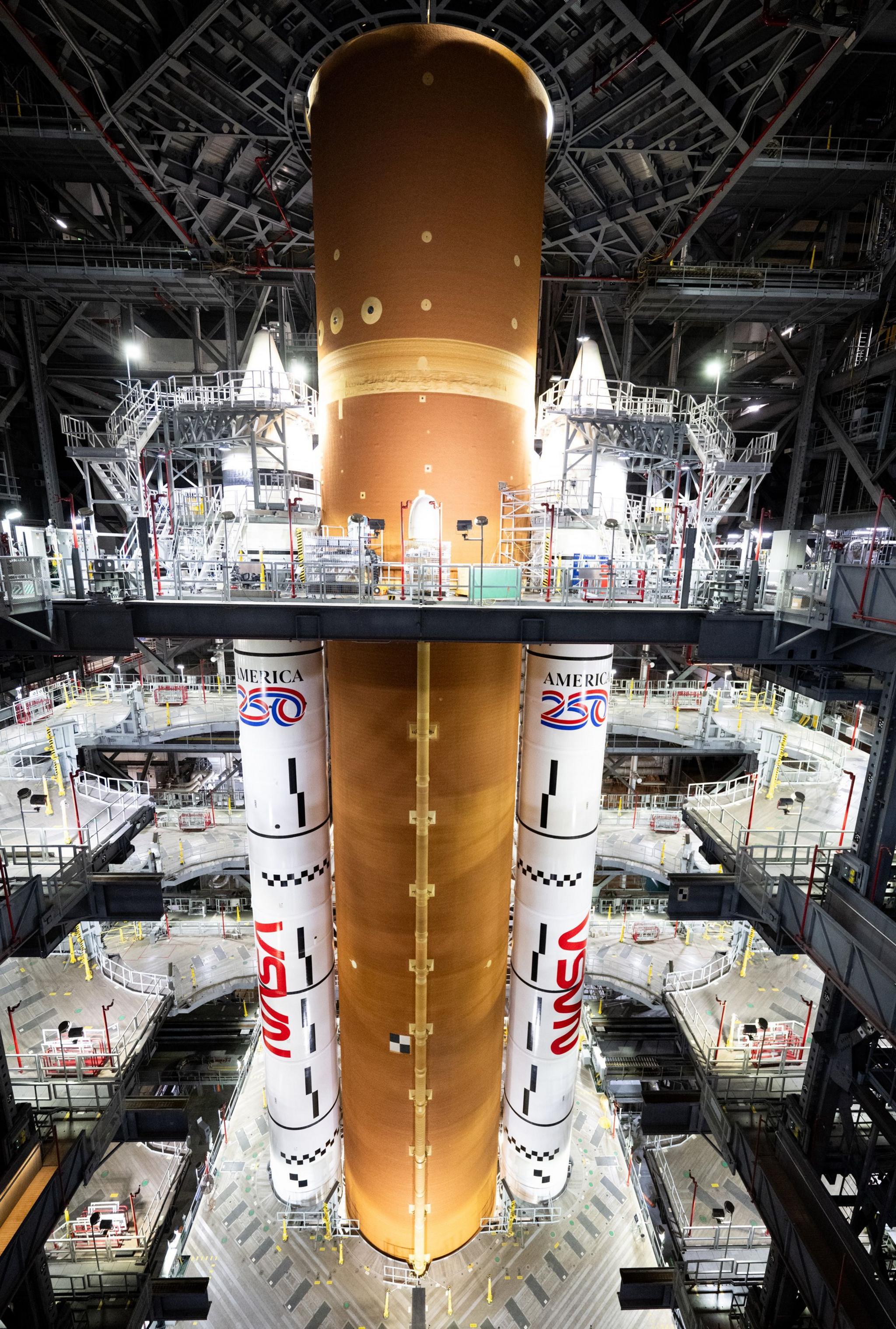 A space rocket, which looks like a giant orange column with white rockets either side, in a tall storage facility