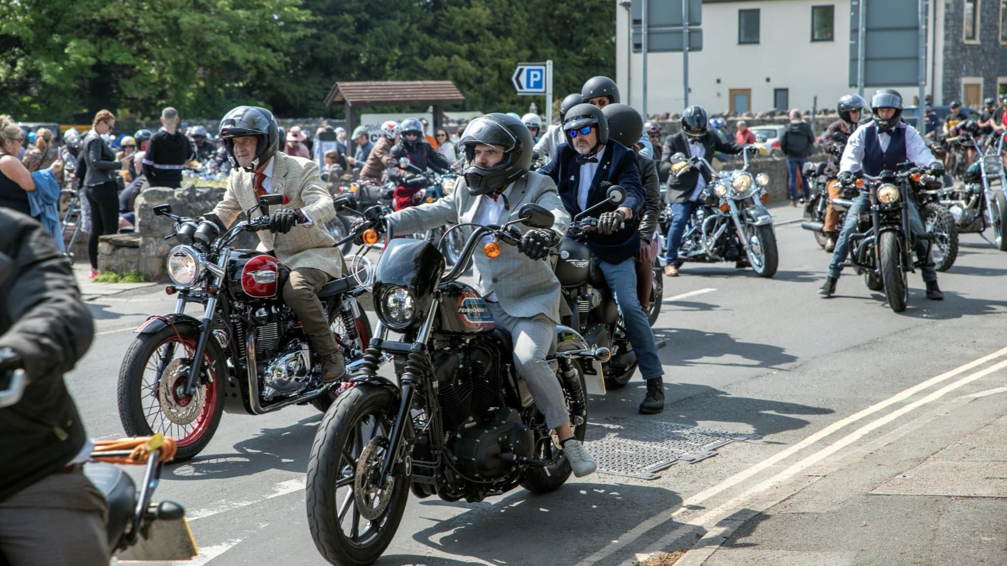 Men wearing suits sitting on motorcycles driving down the road