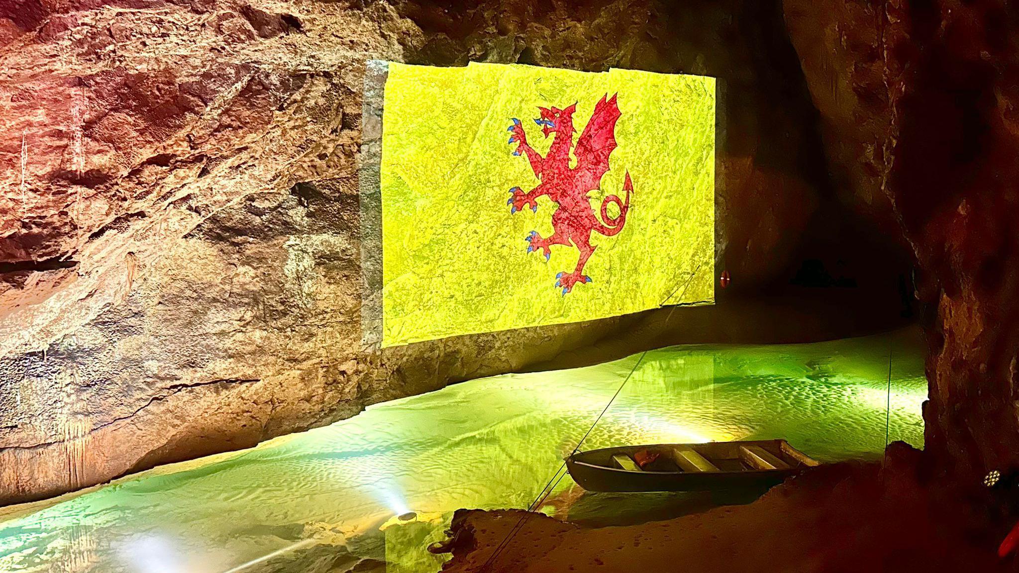 The Somerset Flag is cast onto the walls of a cave. There is water below it which is lit up green.