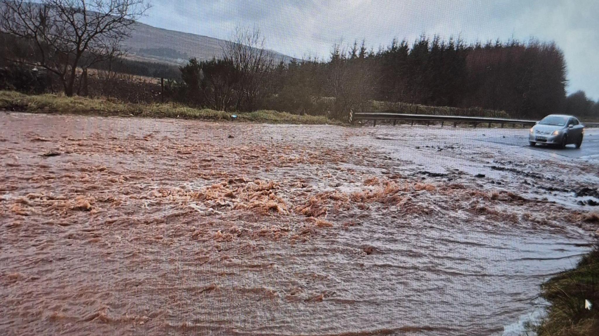 The Glenshane Road in Dungiven covered in flood water. a car sits to the right in front of flood water