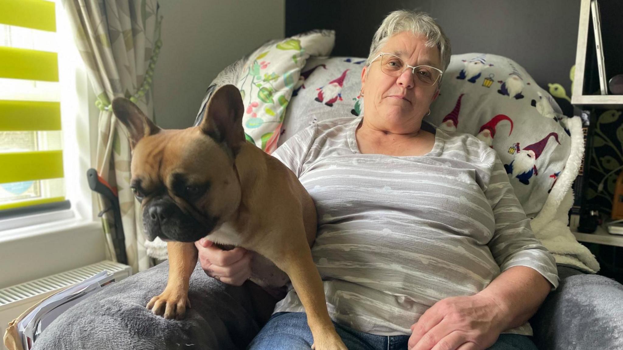 A woman sits in an arm chair with a dog on her lap