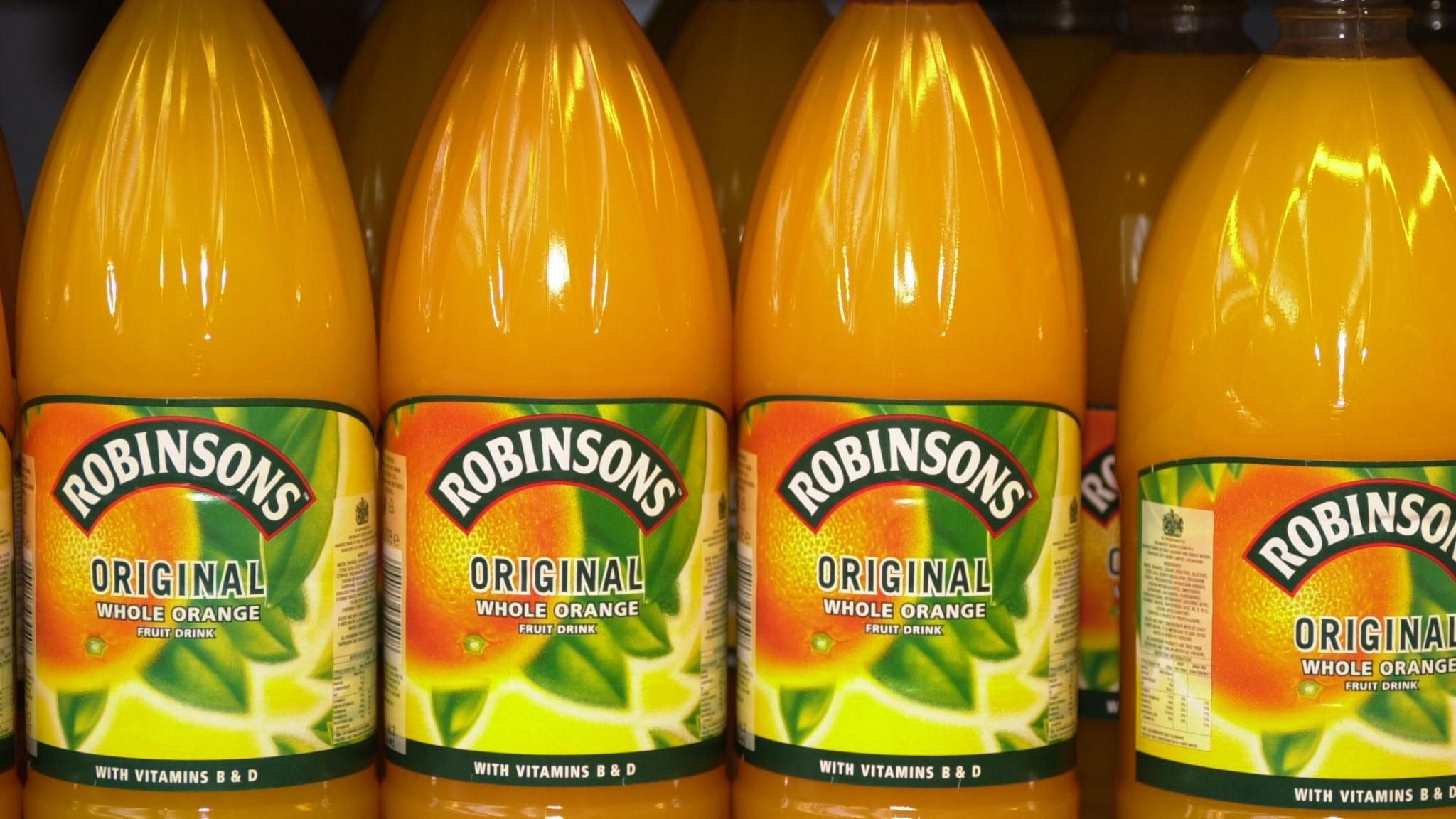 A close-up of bottles of Robinsons orange squash lined up on a supermarket shelf.