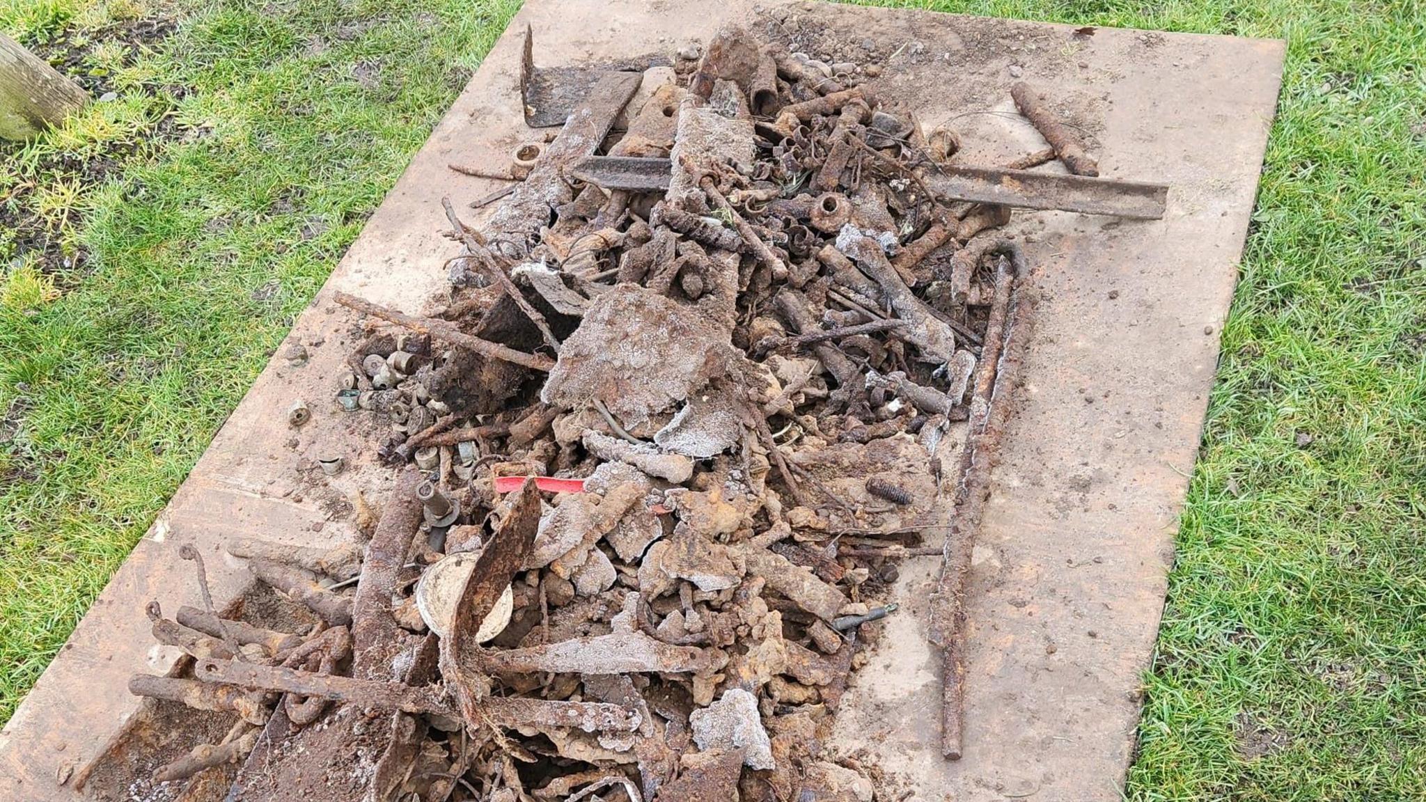 A metal panel laid down on the grass contains lots of metal objects and debris dug up from the park.