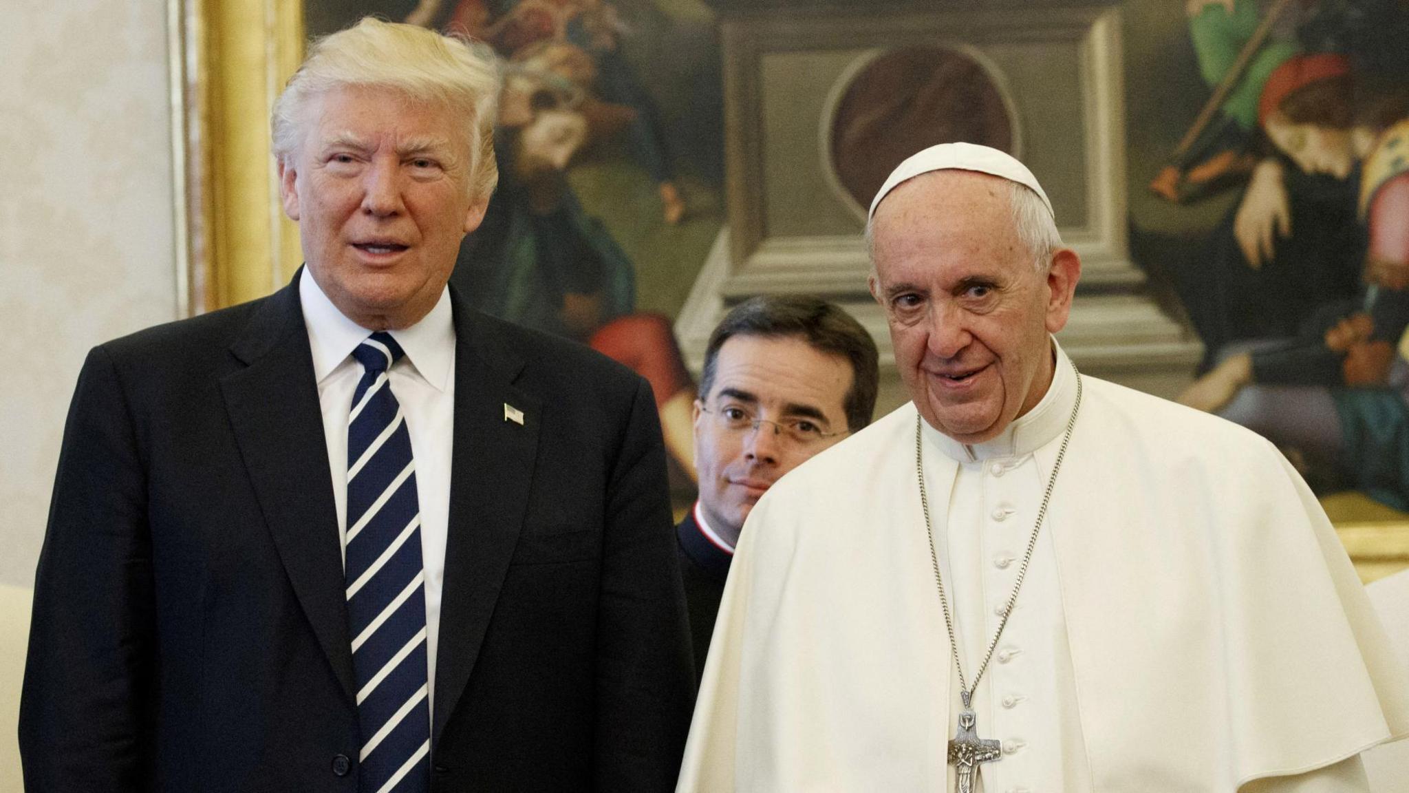US President Donald Trump, wearing a suit, and Pope Francis, dressed in papal guard, stand beside each other while being photographed in the Vatican