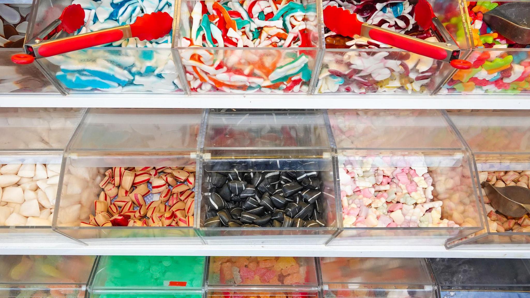 Boxes of sweets for a pick'n'mix, including two red-handled tongs, and on the right of the picture, two metal sweet scoops 