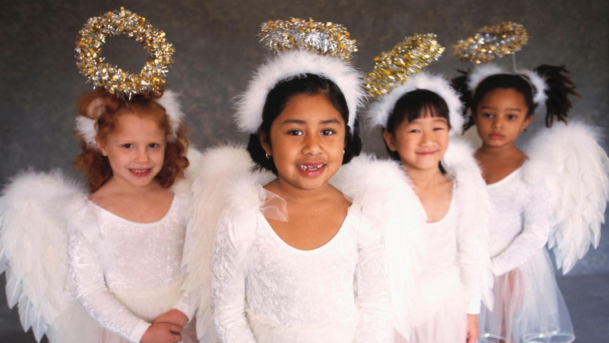 Four girls dressed up as Christmas angels wearing halos and wings.