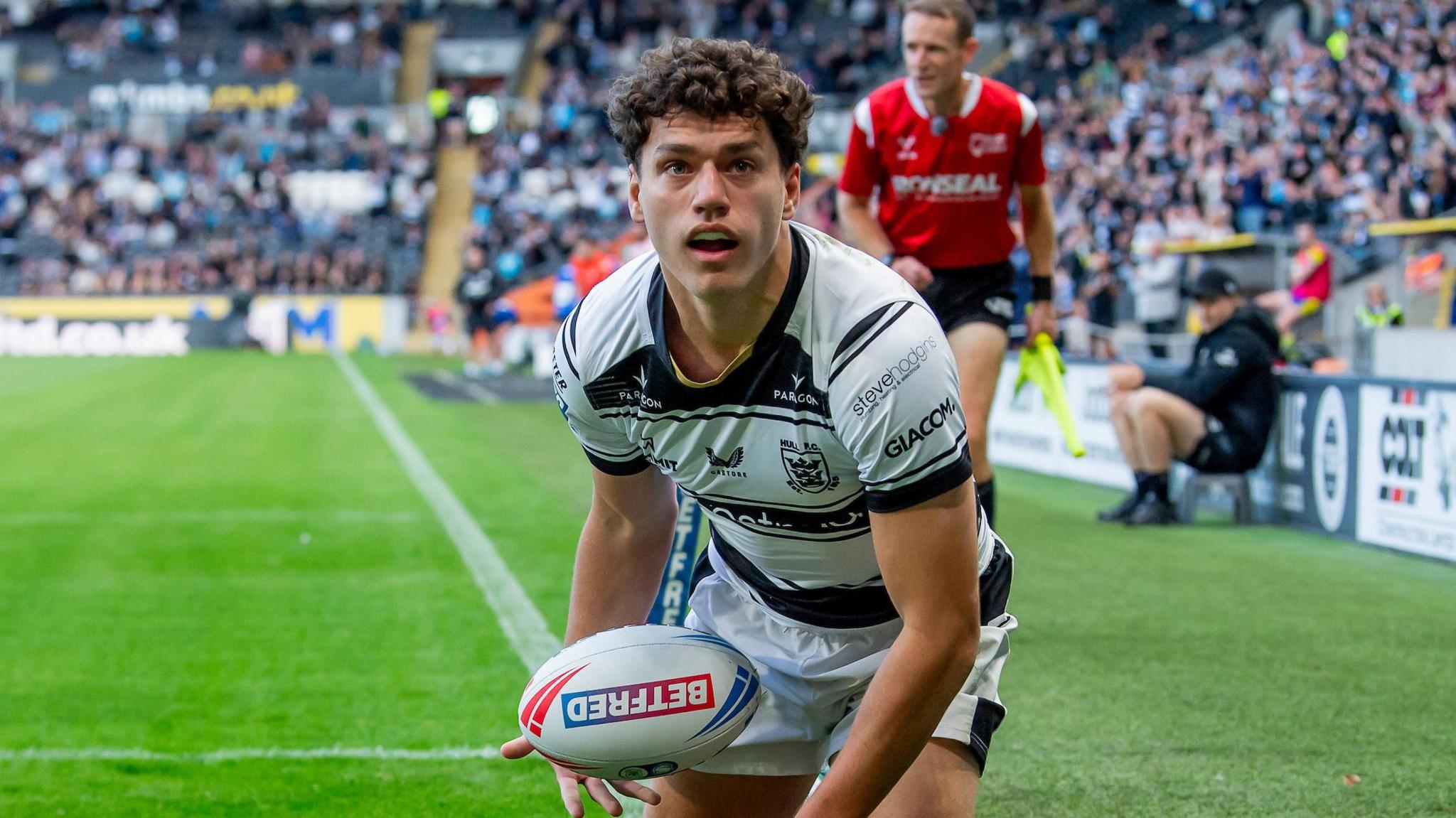 Young rugby player Lewis Martin in Hull FC kit, smiling during a contract signing ceremony with club officials.