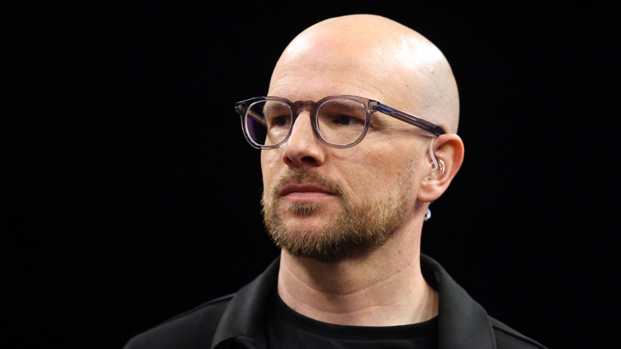A close up of Mark Webster in dark shirt and jacket wearing spectacles and a TV earpiece
