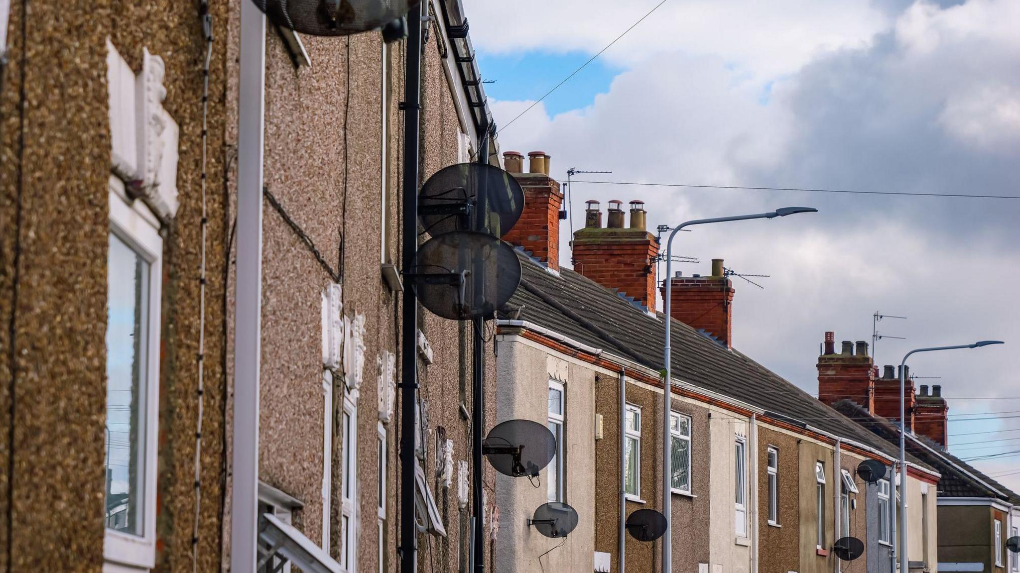 A row of terraced houses. The sky is blue with clouds.