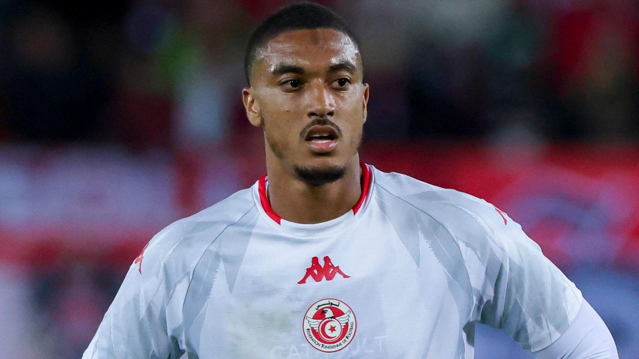 Yan Valery wearing Tunisia's white home shirt with red trim on the neck and Tunisia badge on the centre.