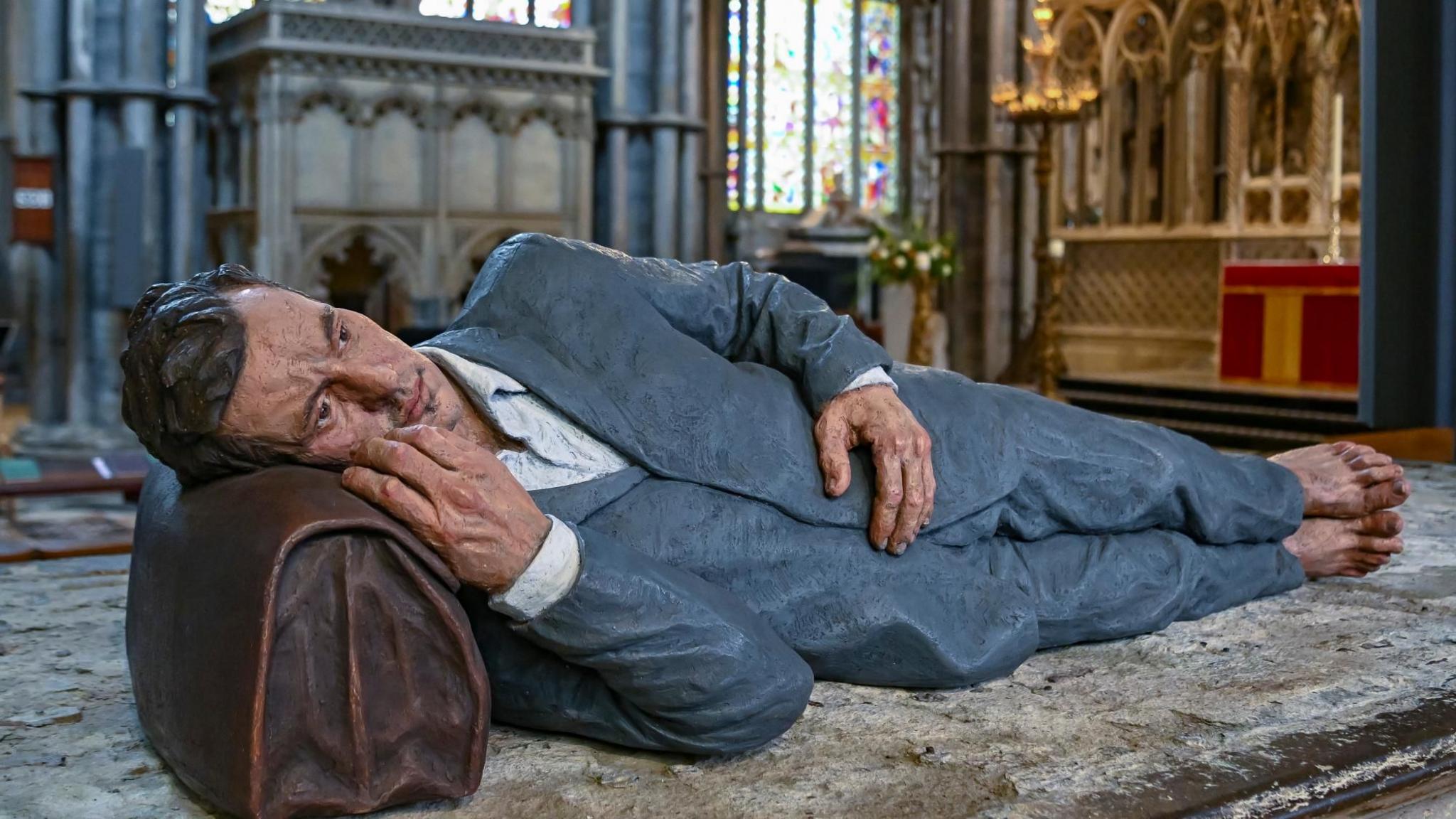 Sean Henry sculpture at Ely Cathedral of a man lying down with his head on a briefcase