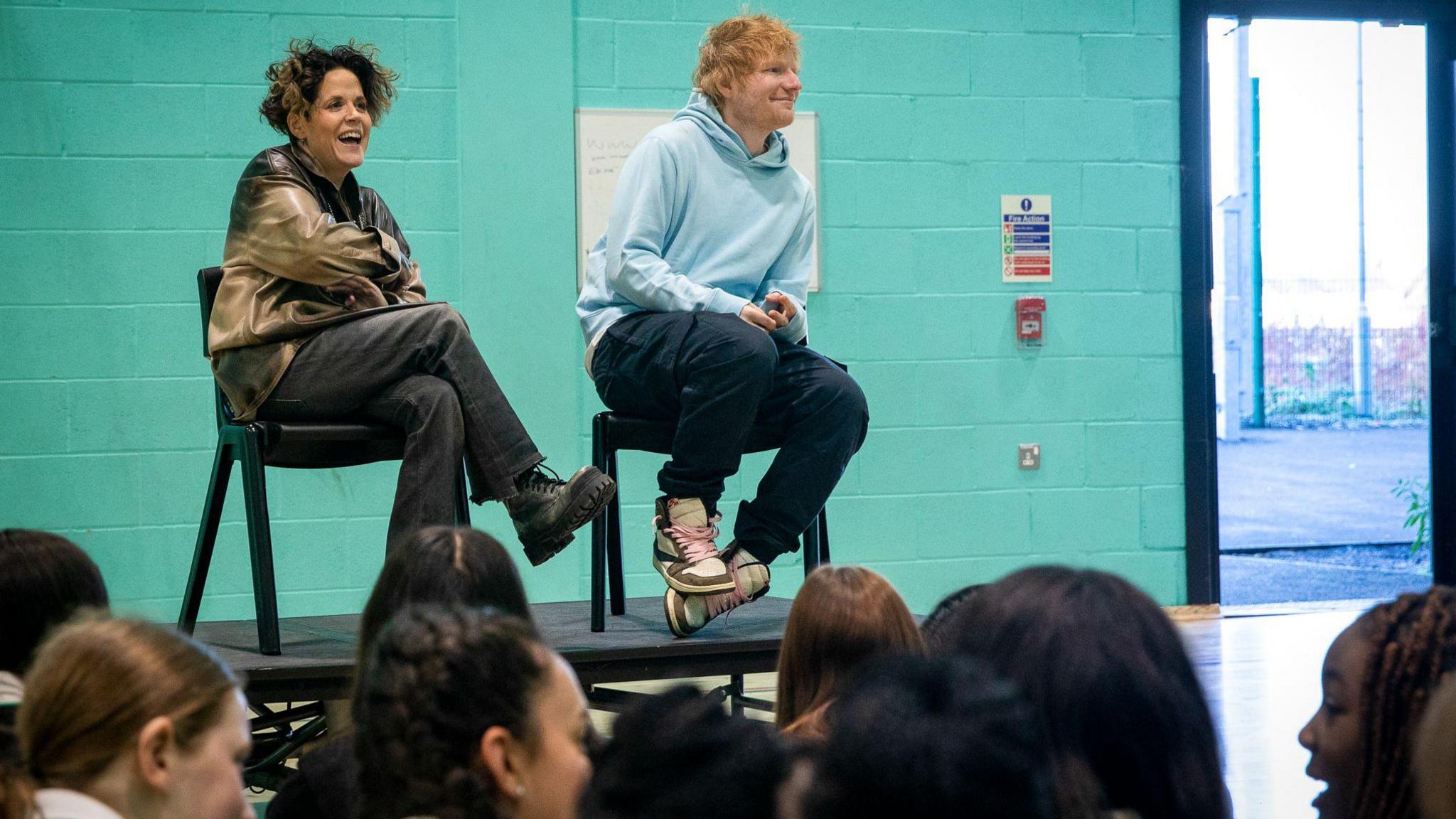 Sheeran and Wadge sitting on chairs on a dais in from of assembled pupils