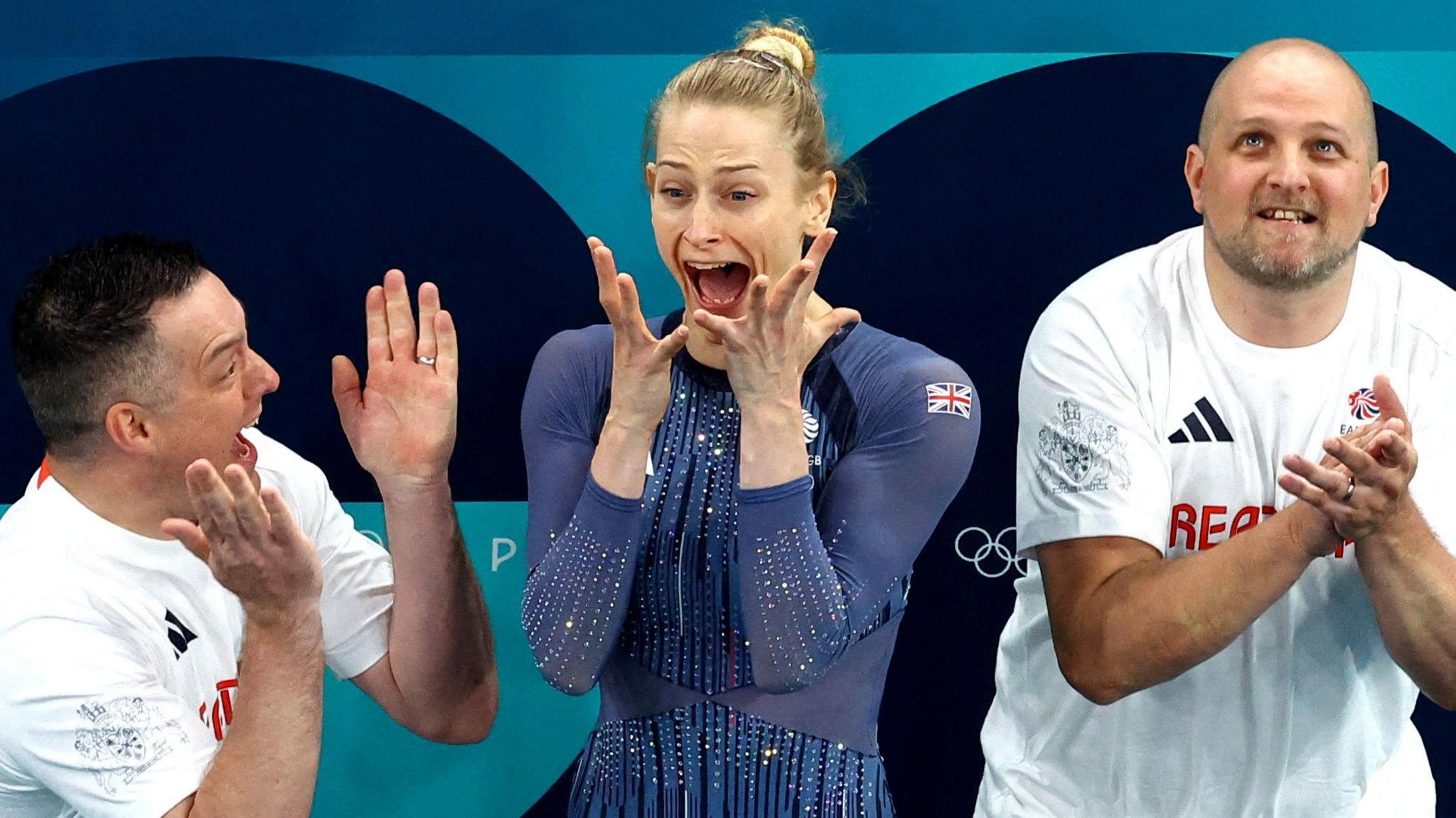 Briony Page and her coaching team screaming in shock as her scores are announced at the Paris 2024 Olympics. Her mouth is wide and she is holding her hands up to her face.