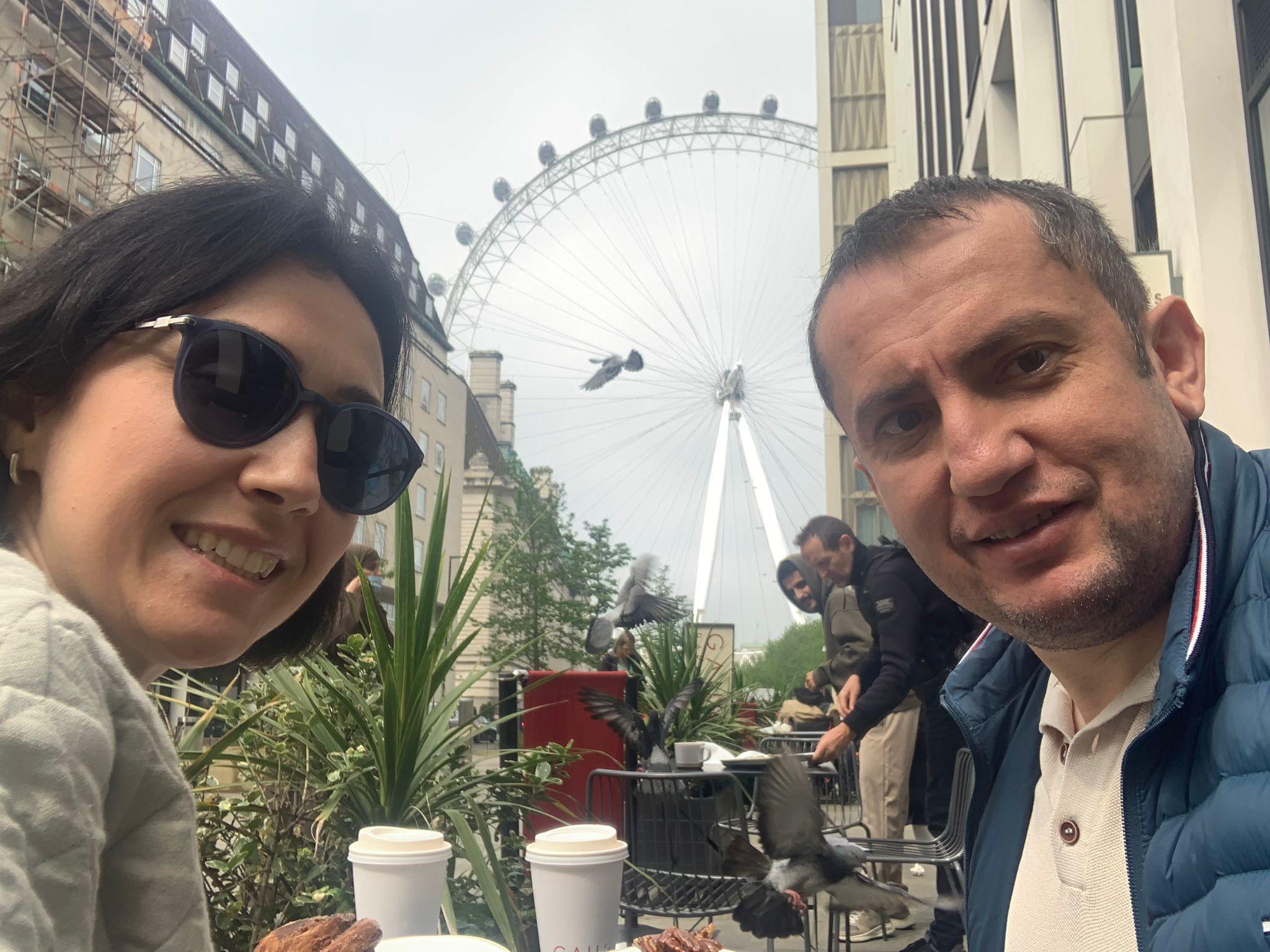 A man and woman sitting having a coffee with the London eye in the background of their selfie
