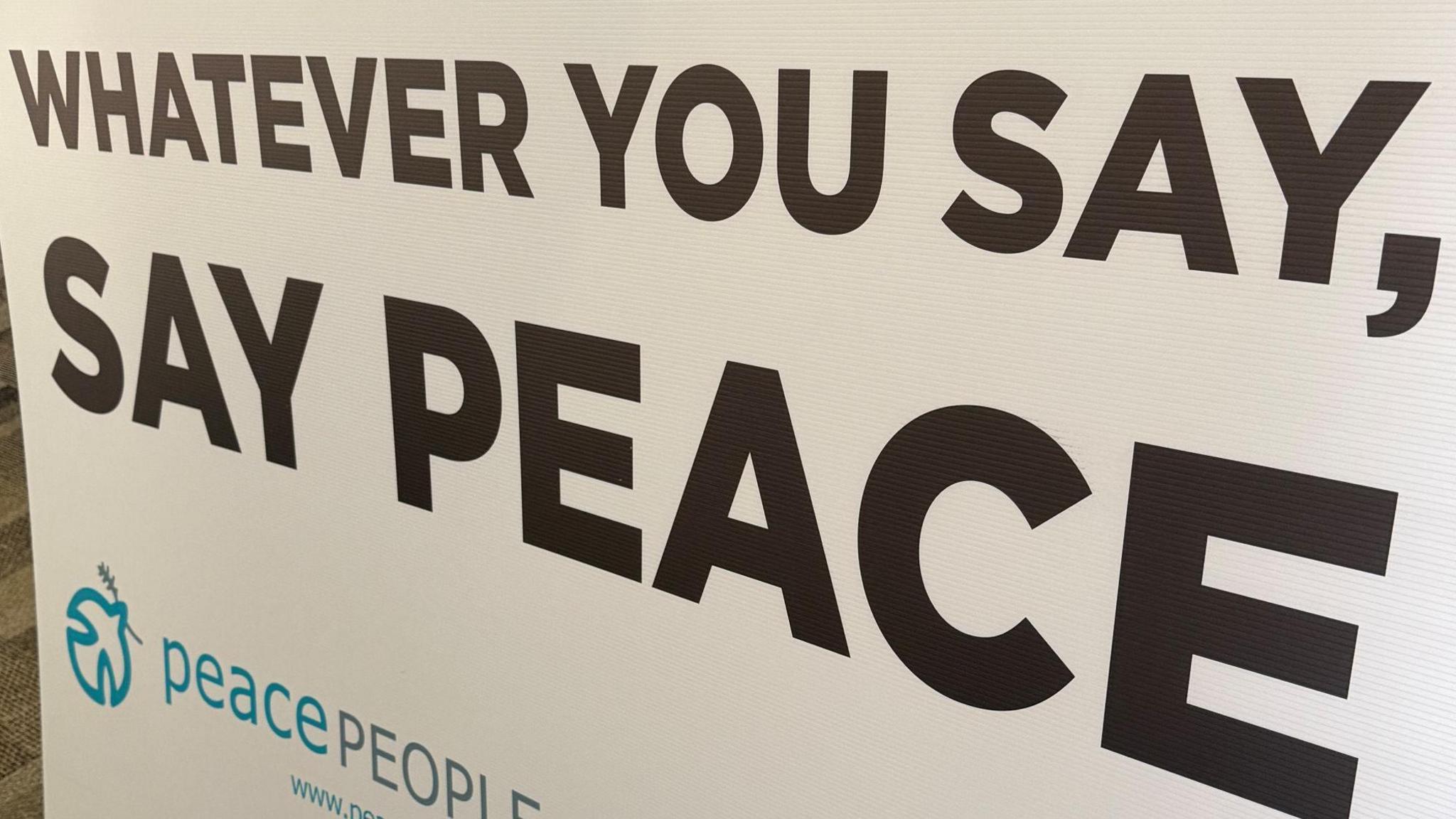 A white board with the words 'WHATEVER YOU SAY, SAY PEACE' printed on it. 