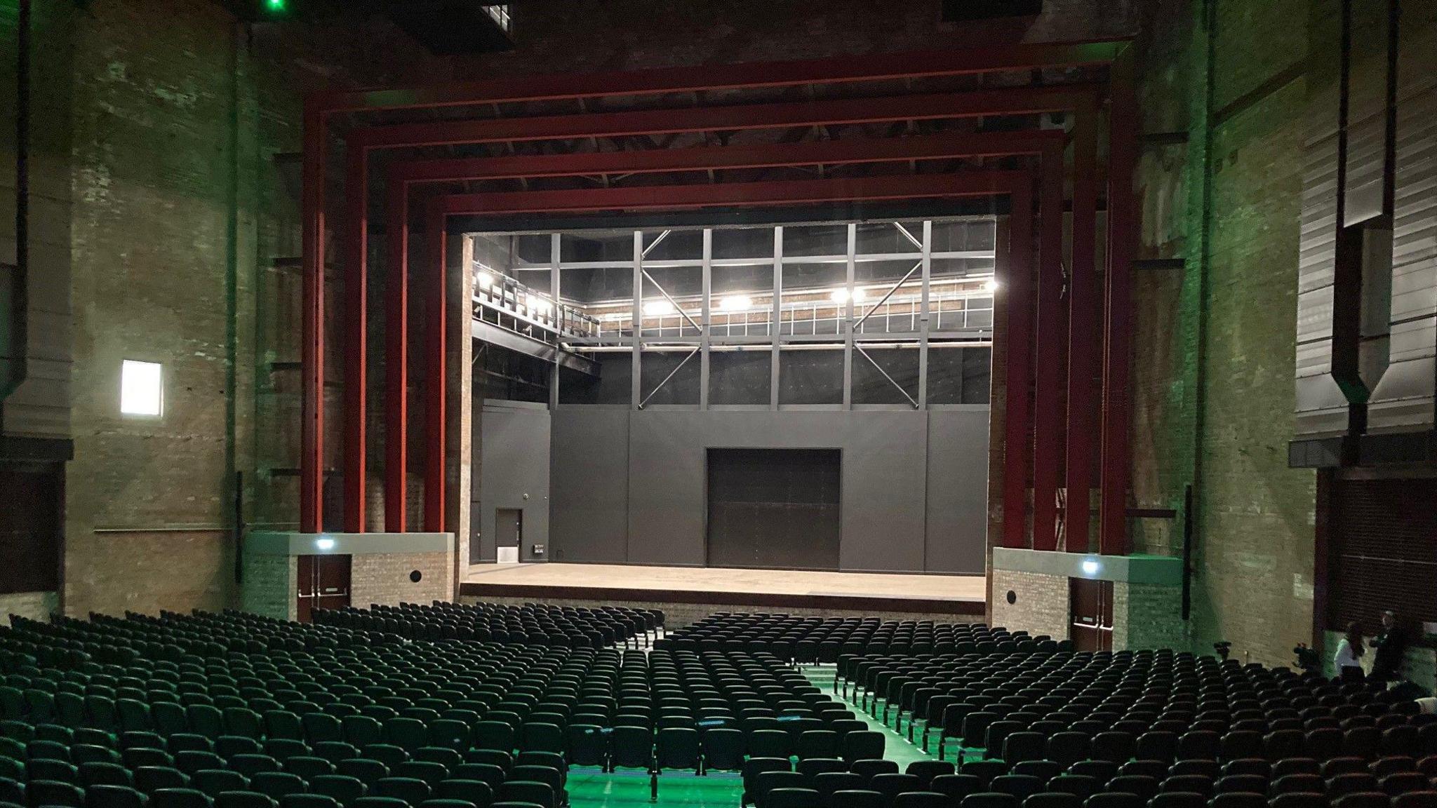 Rows of seating leading towards a stage lit up at the back and surrounded by four red arches.