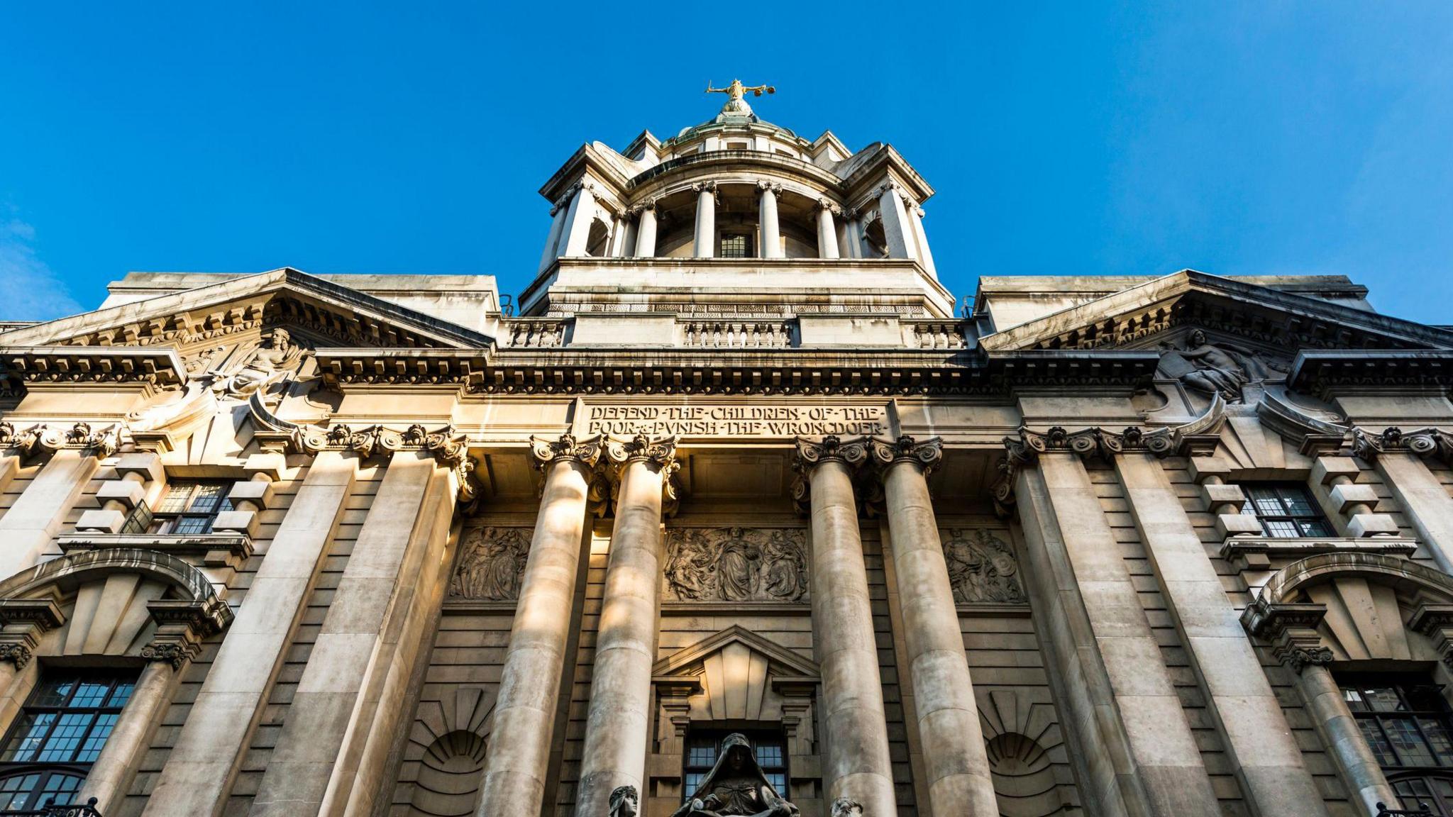 A general view of the outside of the The Central Criminal Court of England and Wales, also known as the Old Bailey. The photo shows an upward angle of the grand front of the building, which is built from sand-coloured stone and is covered with ornate carvings, brickwork and columns. The iconic Justice statue atop the building can be seen clearly.   