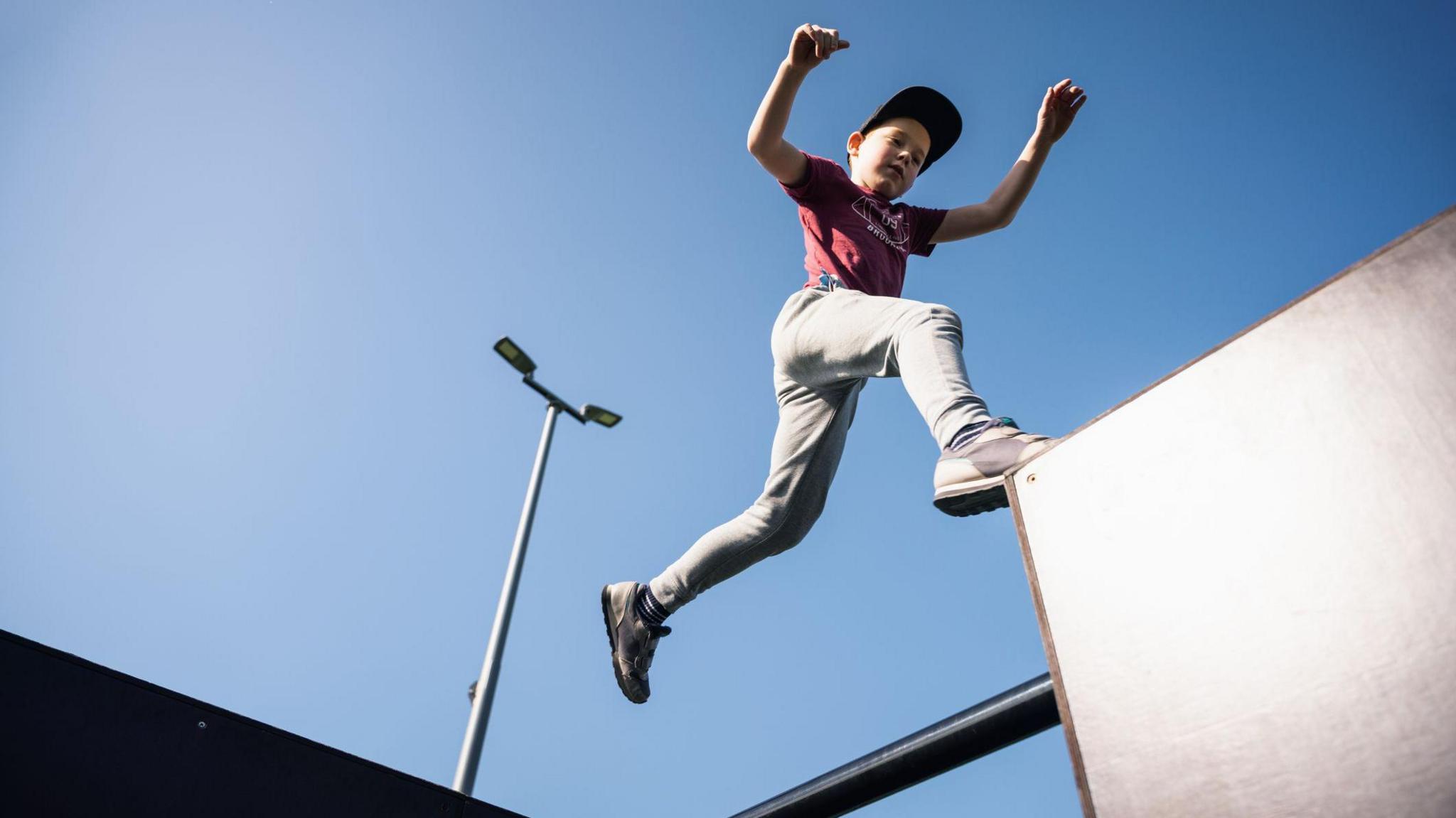 A young child leaps onto a block while doing parkour.