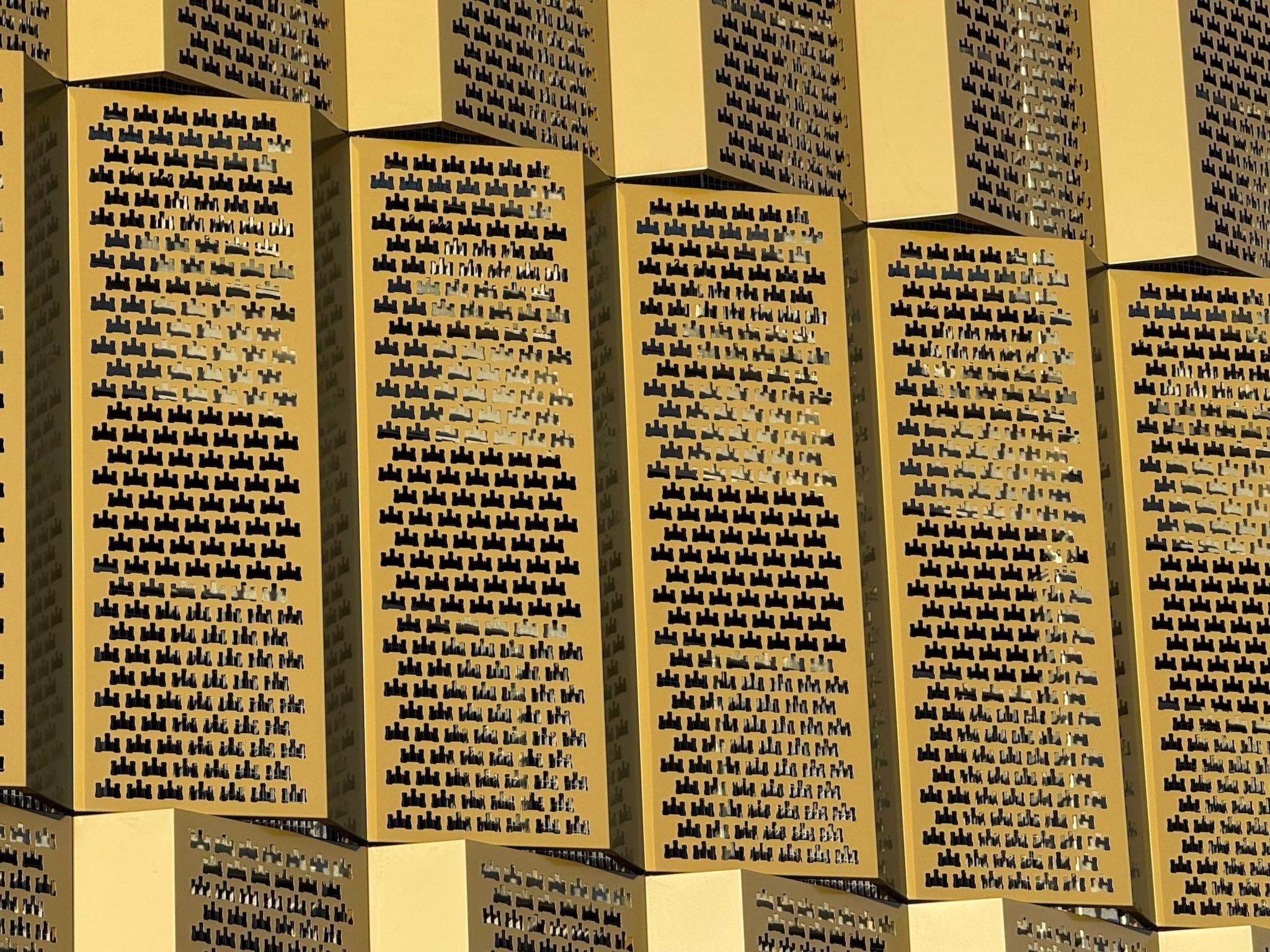 Gold-coloured grills on the side of a multi-storey car park. The panels contain multiple holes which are cut in the shape of a castle.