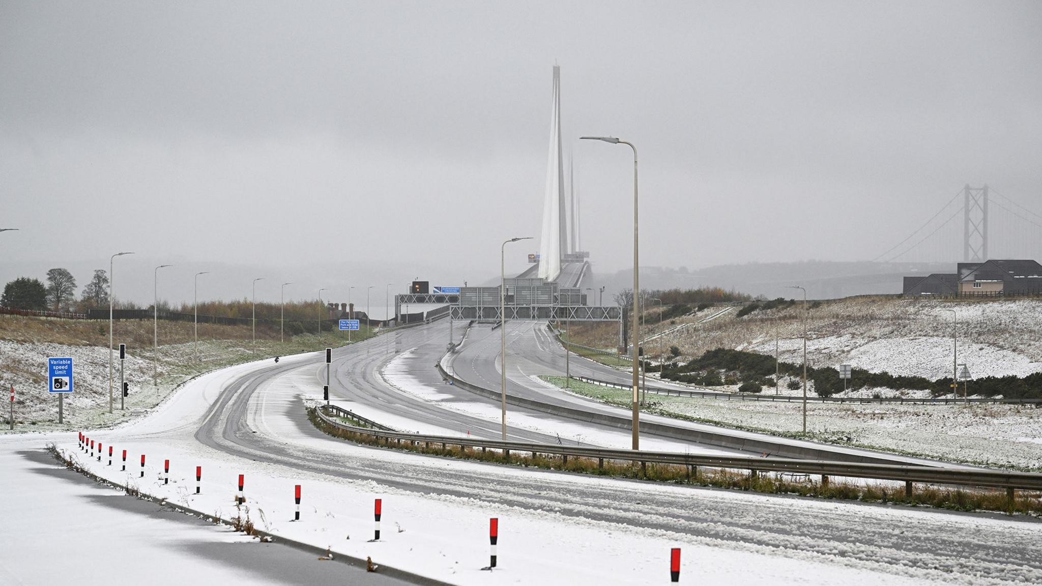 The pillars of the Queensferry Crossing in the distance with an empty motorway covered with snow in the foreground