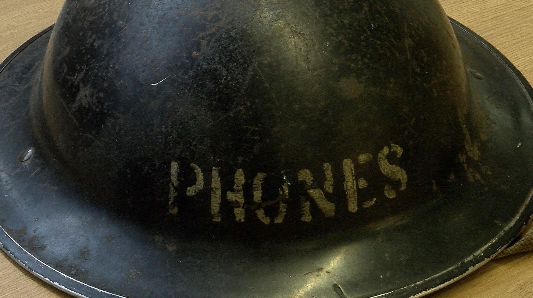 A black tin hat has the word "PHONES" stencilled across the front.