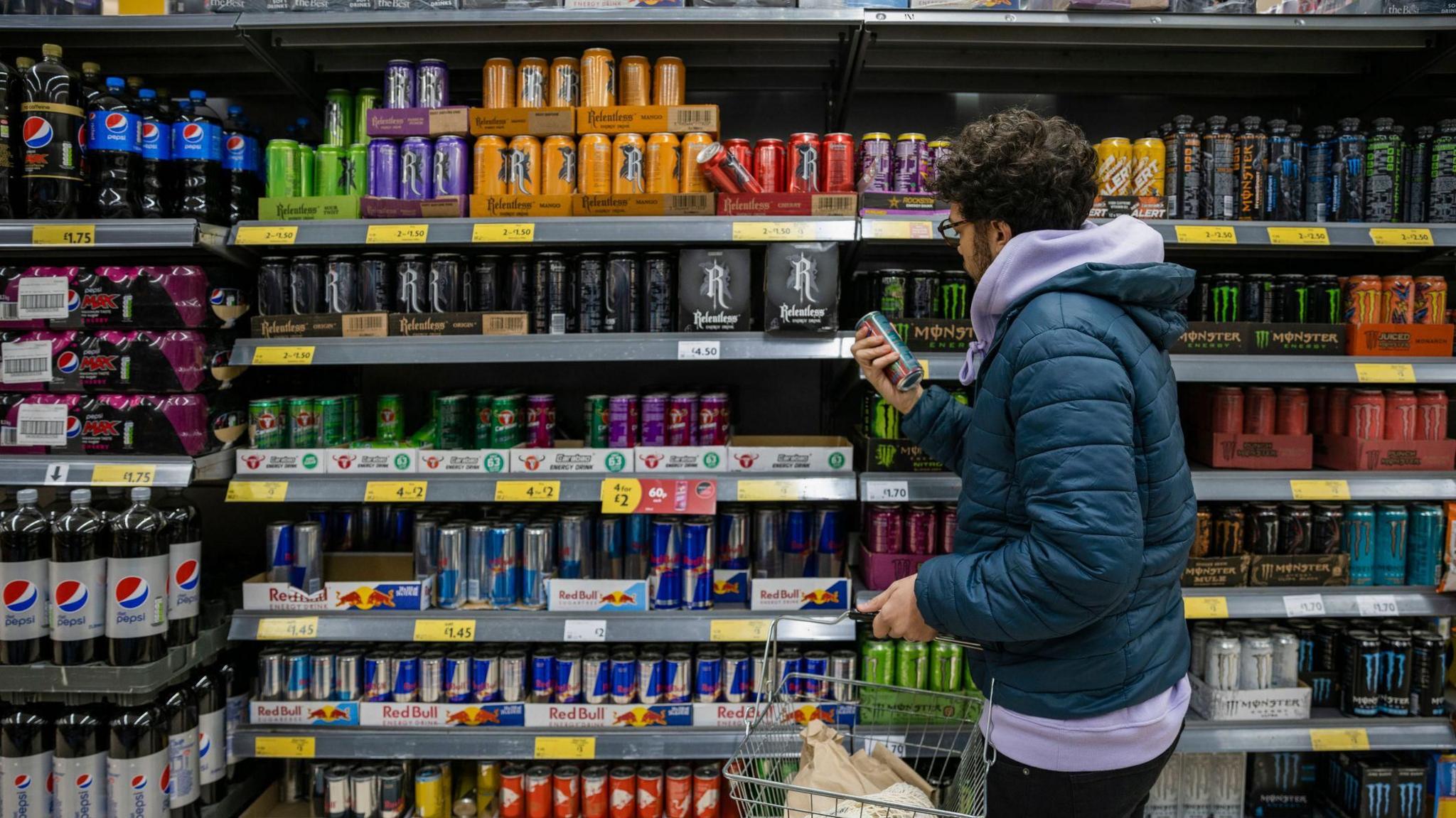 young man picking up energy drink from shelf