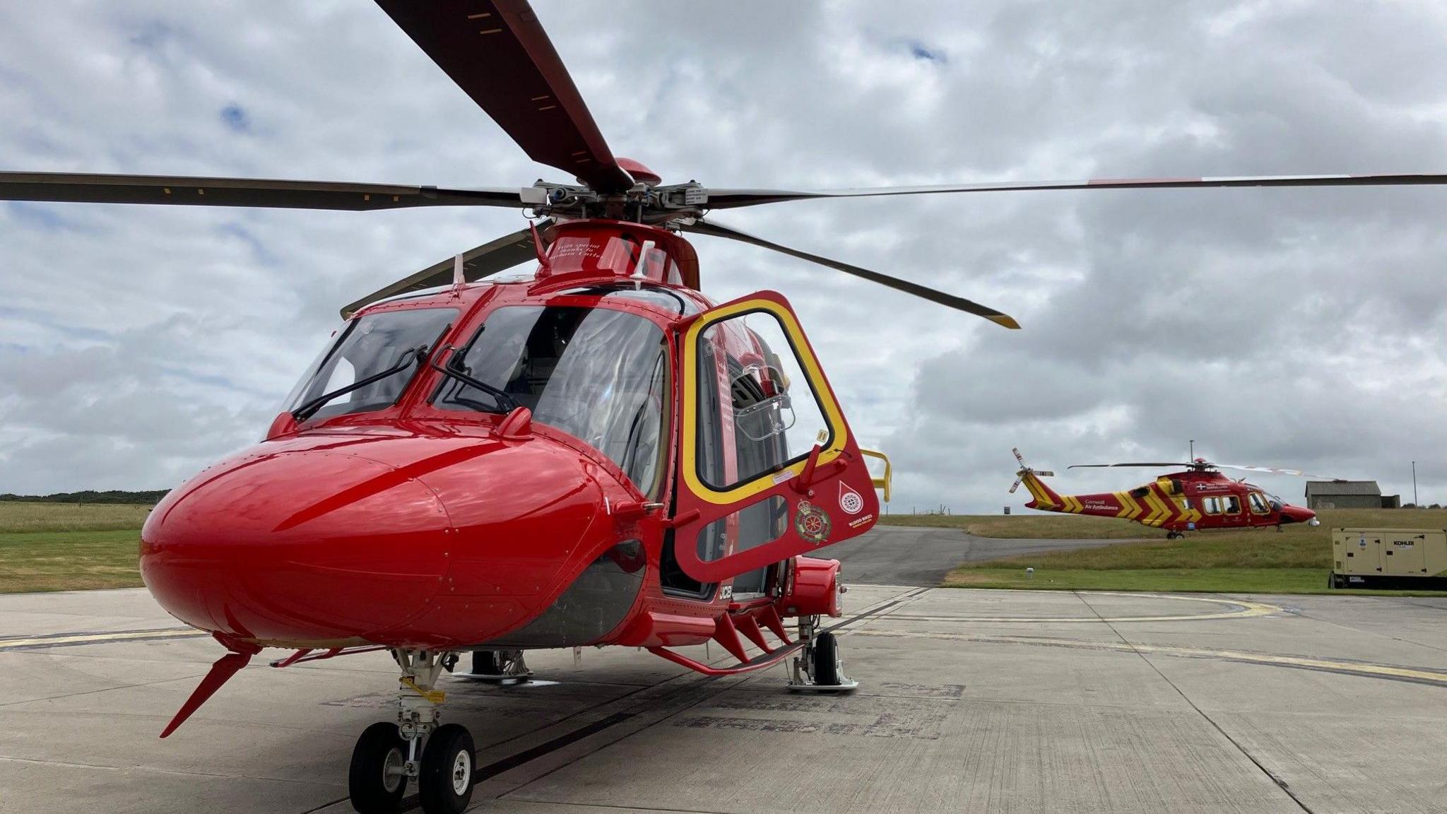 The new air ambulance parked on the landing spot with the pilot's door open and the second air ambulance is parked in the background.