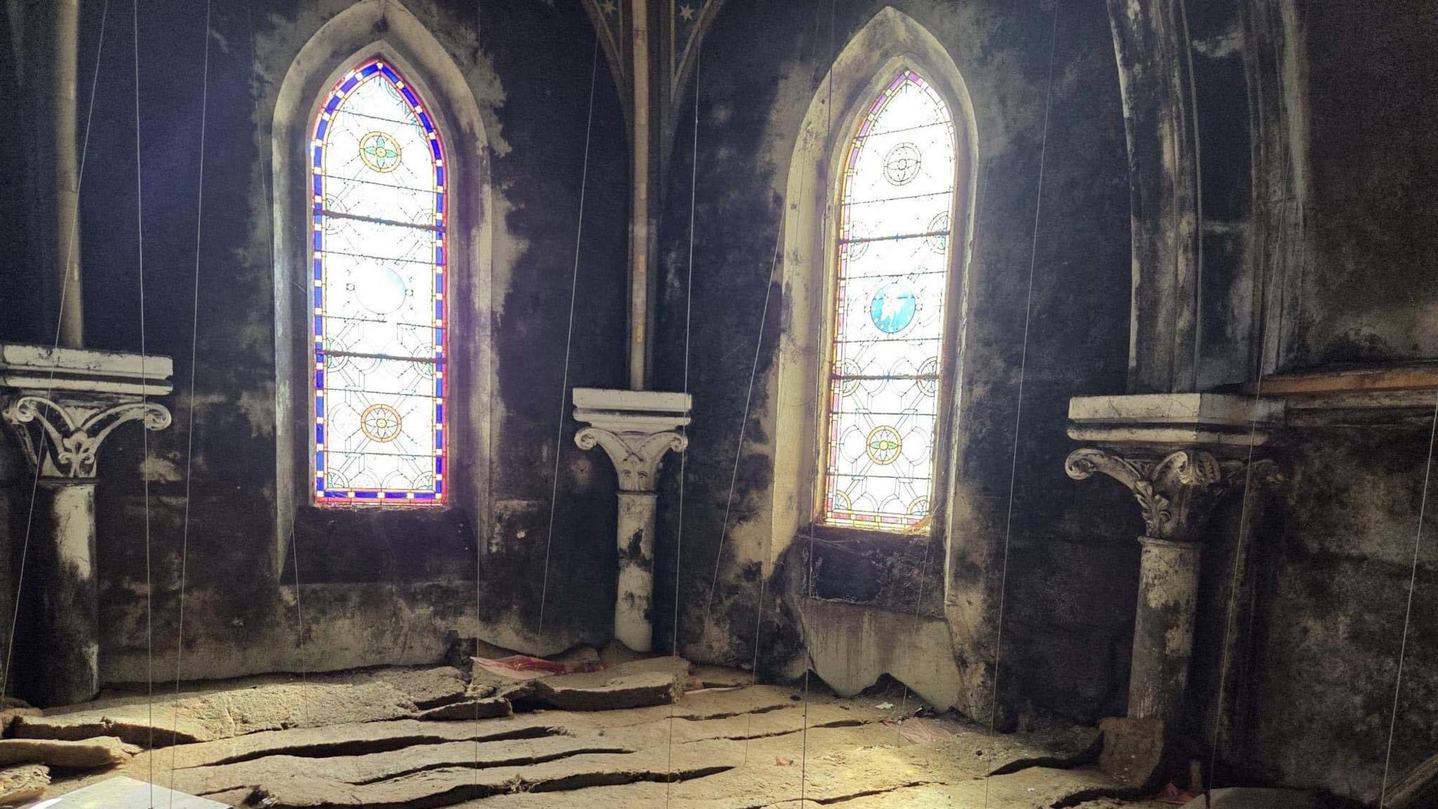 Inside the monastery in Paignton. There are two church windows at the back and the building is dark. The floor is damaged.