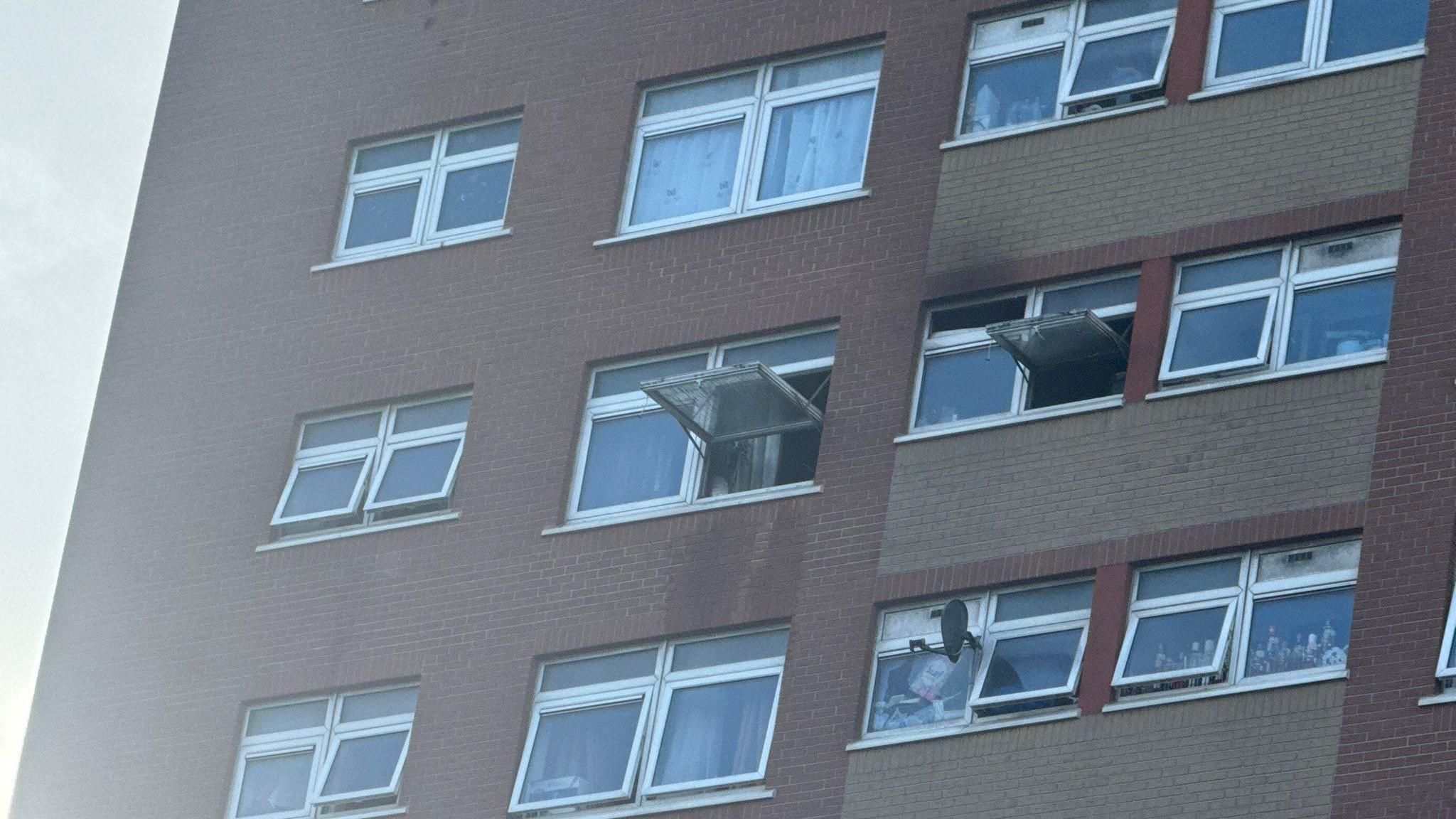 A close-up image of the windows at Croydon House. Both the windows are fully opened and blackened with smoke, and are clearly very high up in the building. There is a very small amount of discolouration visible on the brick above one window as well. 