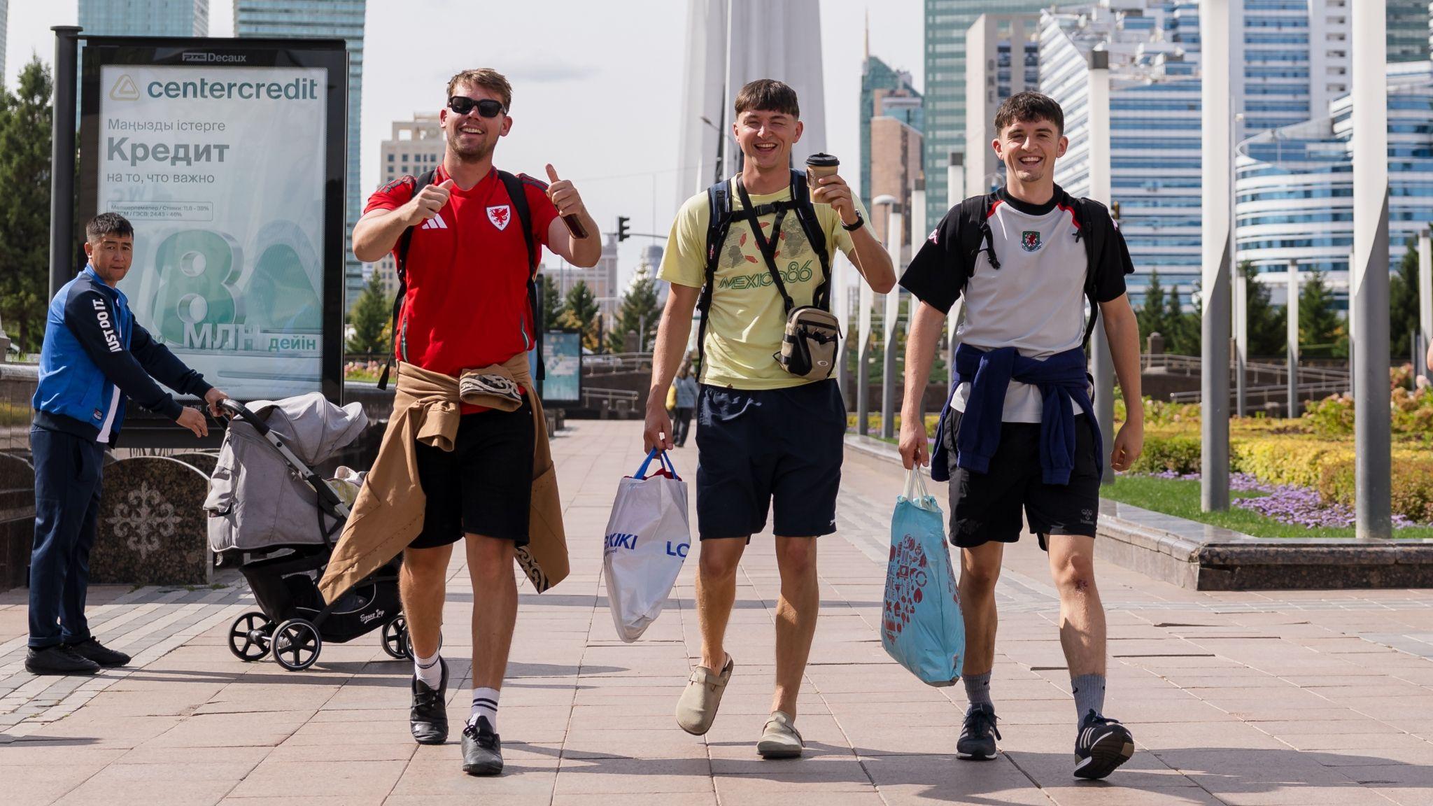 Three Wales football supporters walking with bags and smiling for the camera in Astana